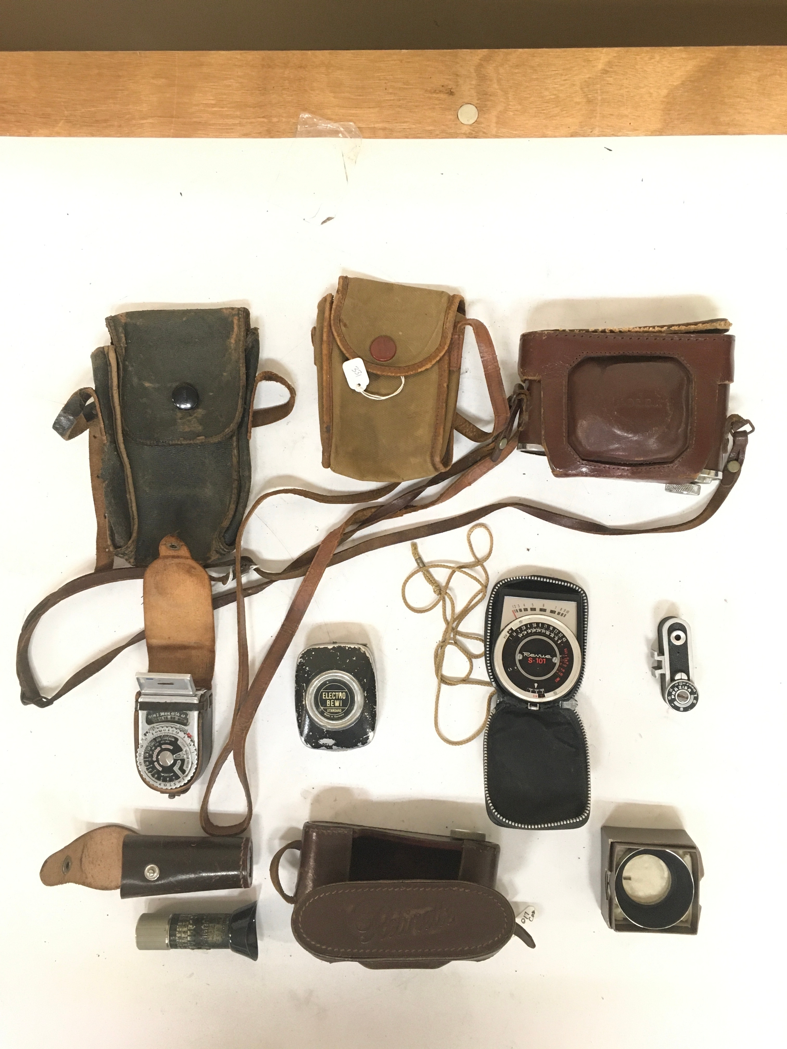 10 items an assortment of 4 empty camera bags/ holsters for various Kodak modals and 1 Butchers cameras bag. 3 exposure meters ; a Sekonic with case,  a Electro Bewi, Revue S-101 with case. 1 Prazisa range finder. 1 Practos Junior camera lens with holster. 1 Durafit lens hood.
