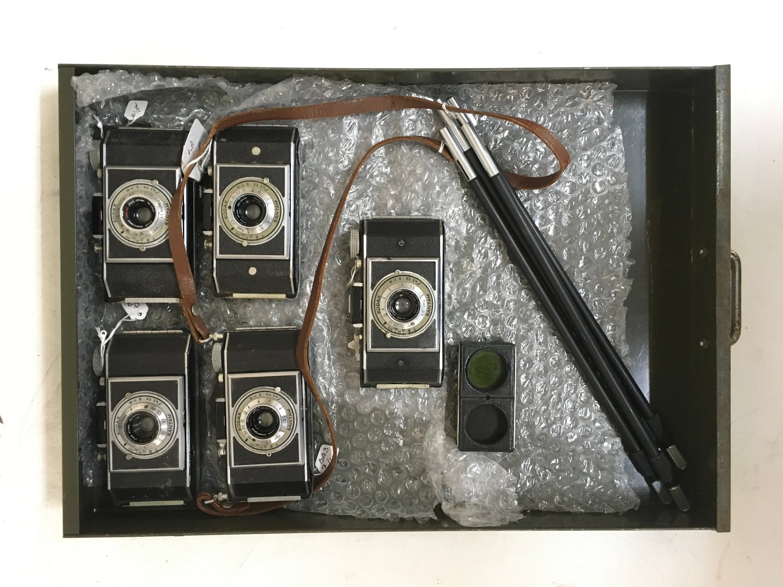 7 items. 5 Kodak Bantam cameras, 1 includes strap. 1 Kodak coloured lens filter. Set of camera brackets/ holder stand.