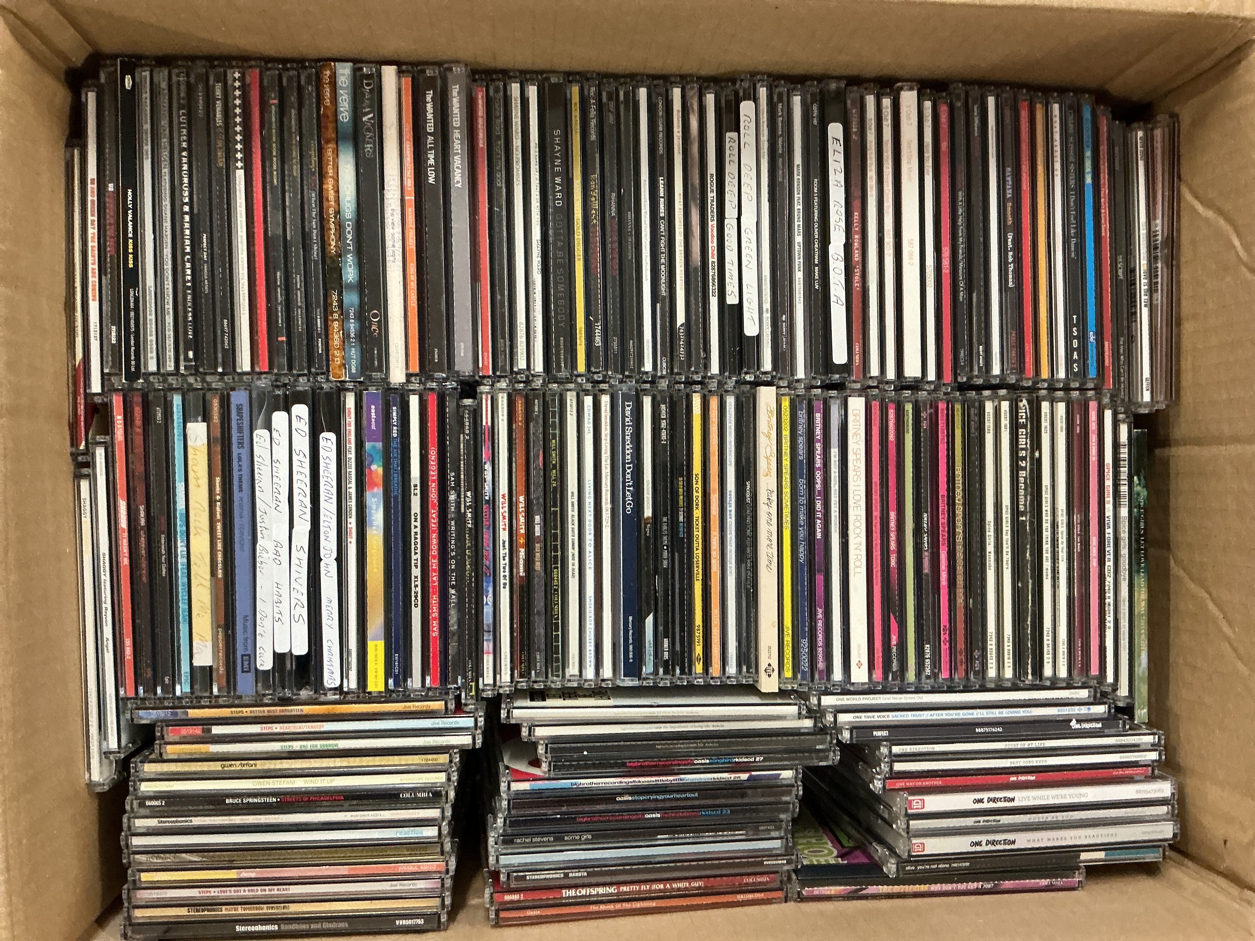 A box and a bag of CD singles by various artists including The Verve, Beyoncé, The Wanted and many more.