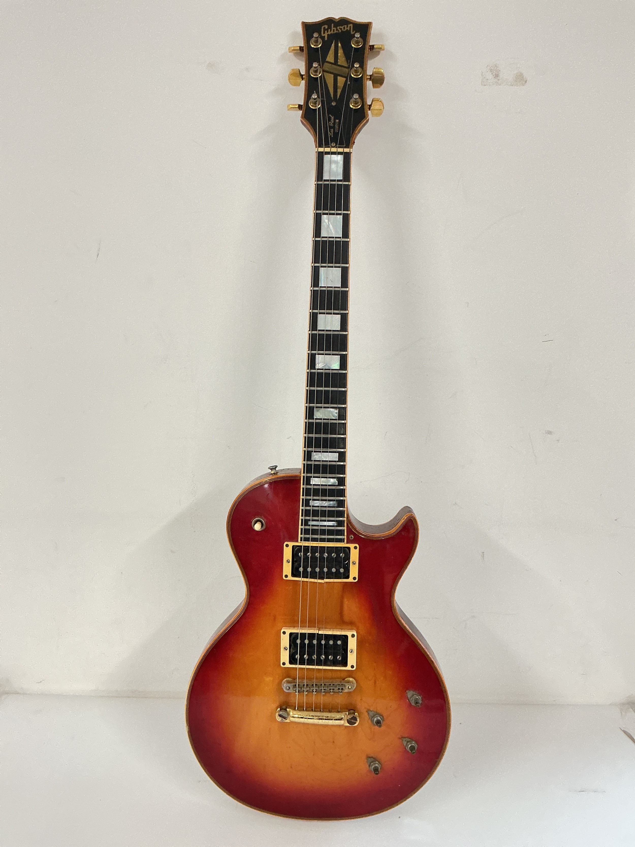 A circa 1970s Gibson Les Paul Custom electric guitar in a sunburst finish, serial number on headstock 730342. Has had replacement.. tuners, missing control knobs, damage to pickup housing. Looks like the back of the neck has heat damage. Needs attention. Comes with a hard shell Gibson branded case and a box of accessories.