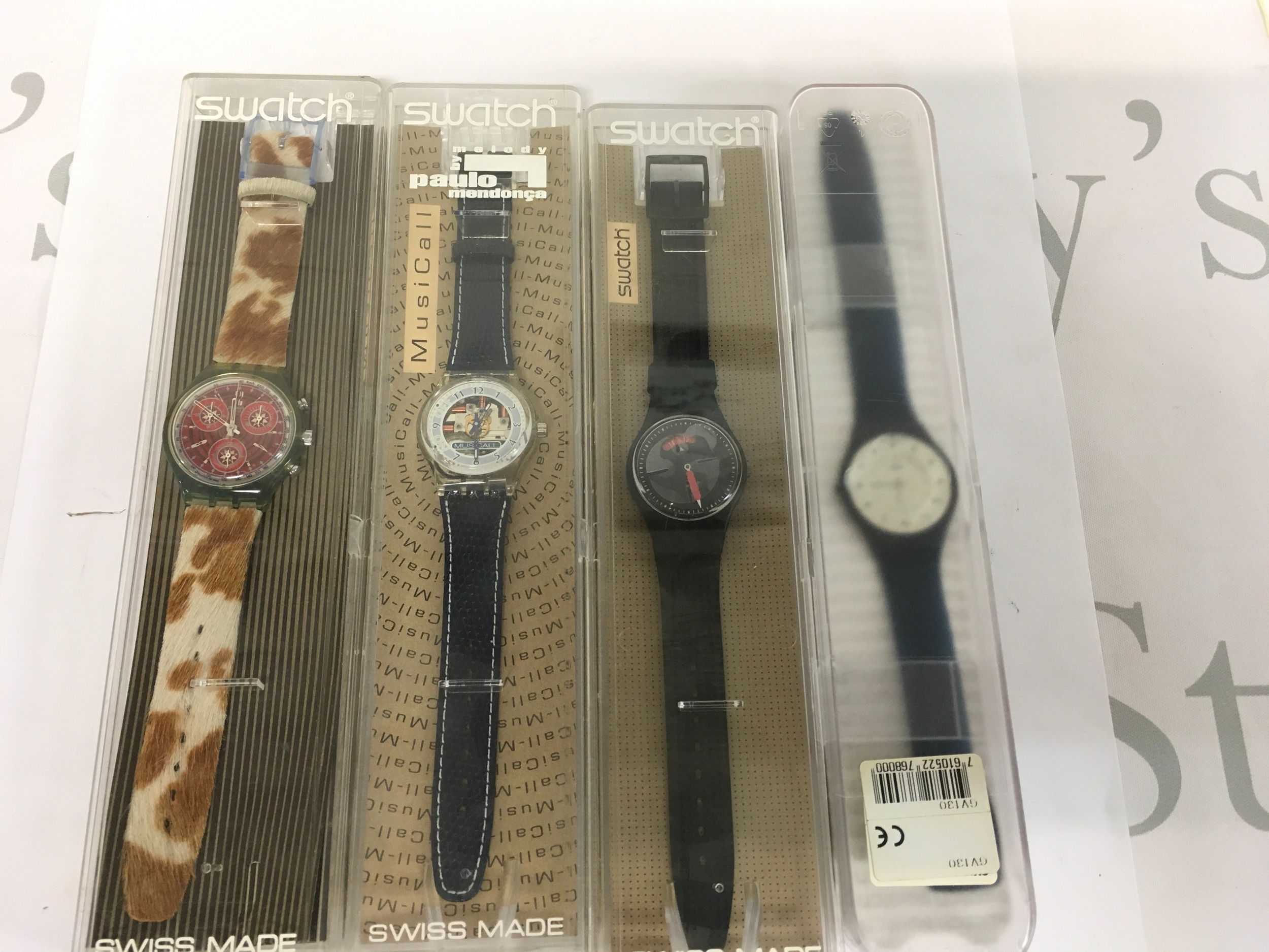 Four vintage Swatch watches come in their original blister pack packaging. The set includes a mix of designs, such as a cow-patterned chrono and a black model from the early 1990s.