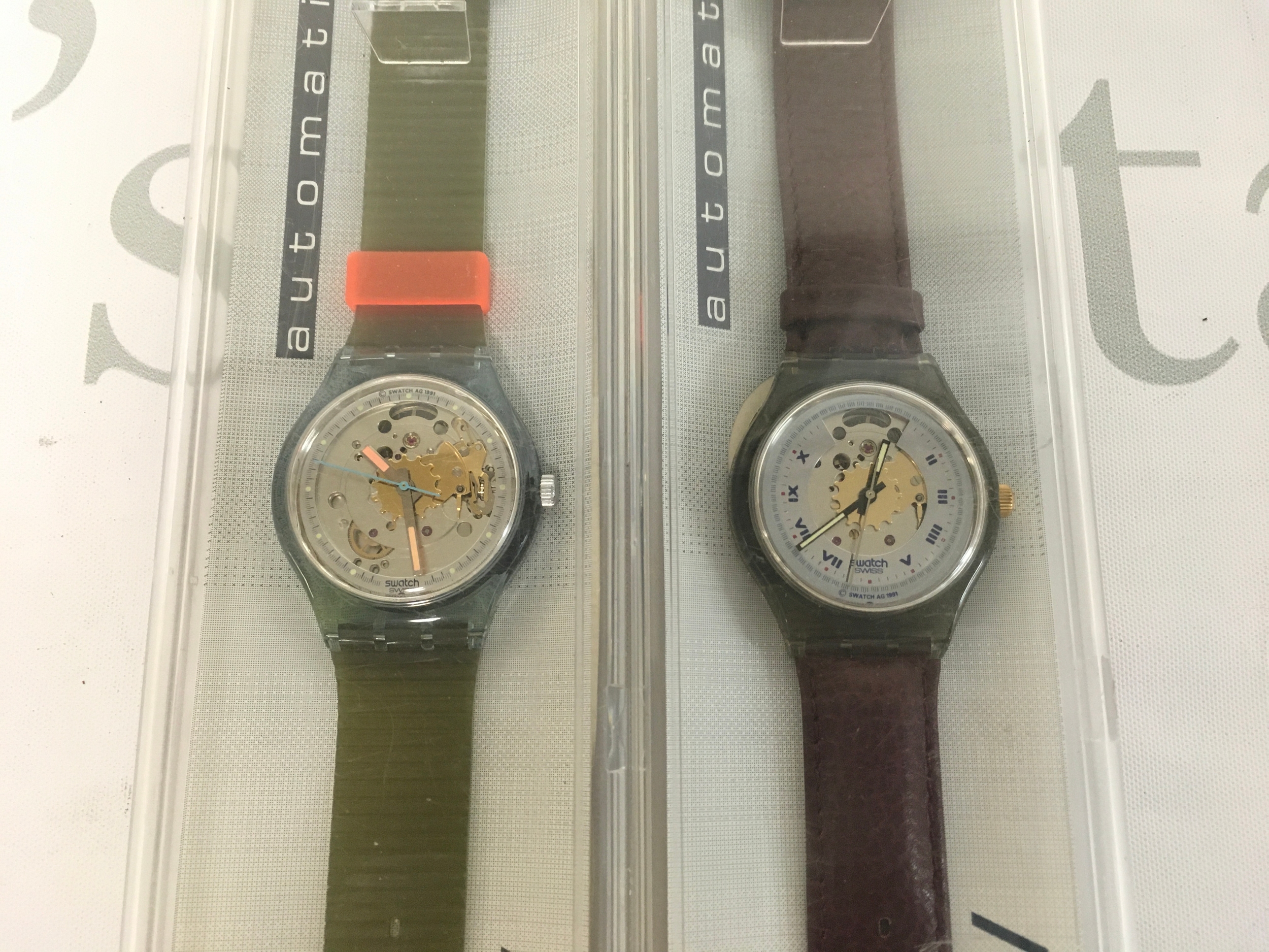 1991 Swatch Automatic watches, featuring a 37mm skeleton dial design. The watches are from the vintage Originals Automatic collection and include their original display packaging. The model on the right is the Swatch Rubin (SAM100) with a dark leather strap and gold skeleton details.  