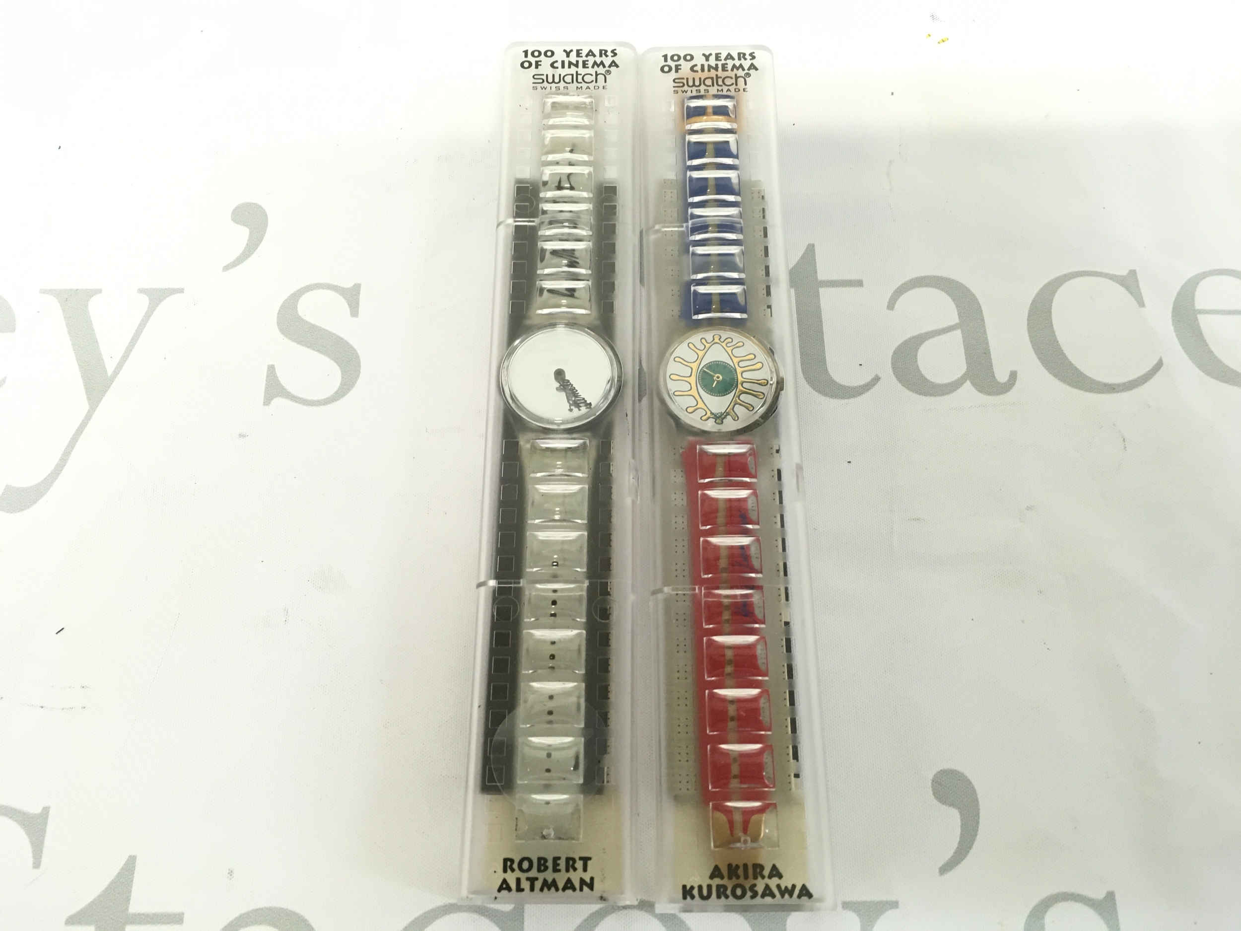 Two Swatch 100 Years of Cinema limited edition watches from 1995. The watch on the right is the GZ141 Eiga-Shi model designed by director Akira Kurosawa, featuring a distinctive eye graphic on the dial. The watch on the left is designed by Robert Altman.