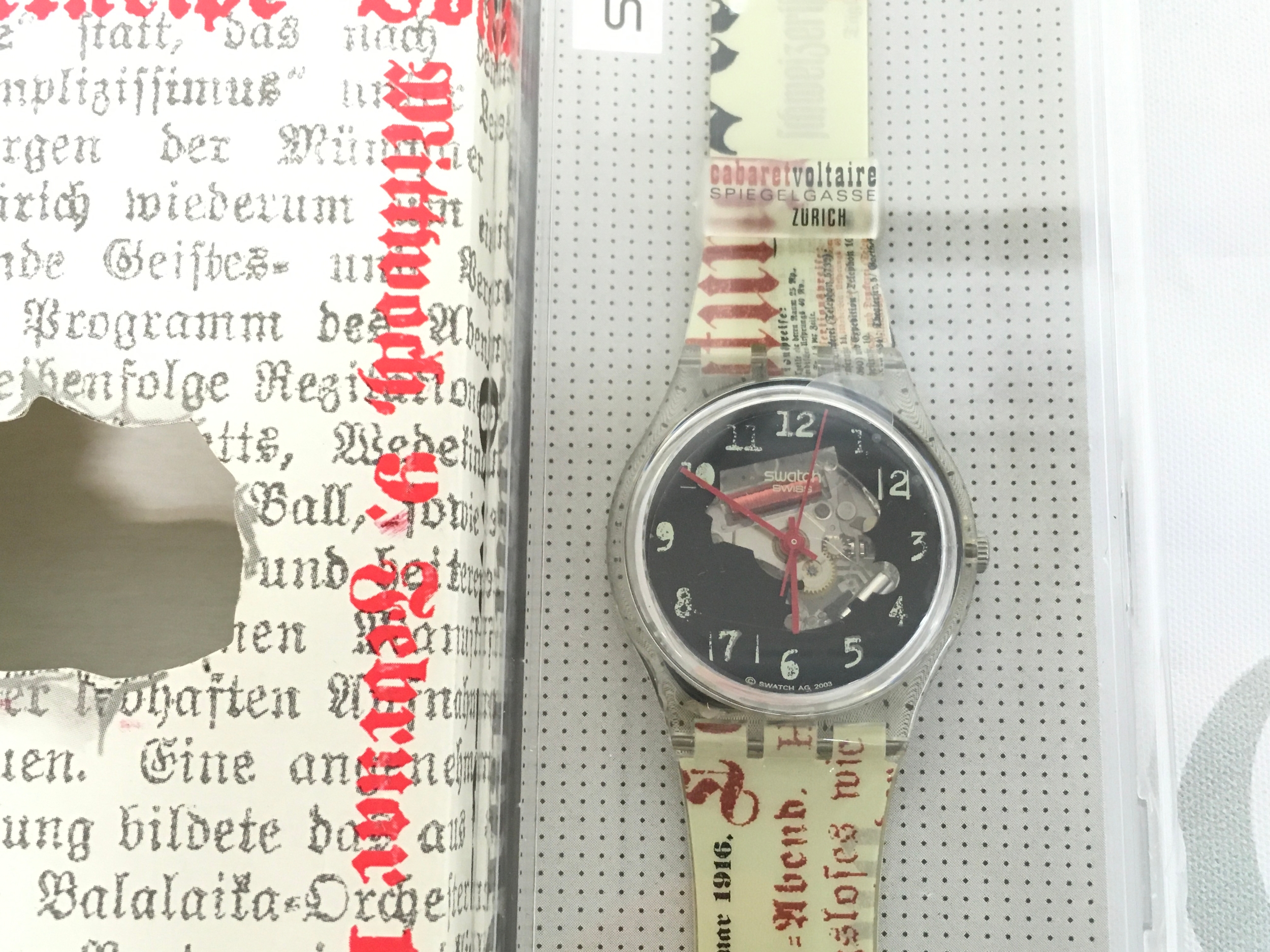 2003 Swatch Special named "Dada Traces" (model GZ184) celebrating the Dada art movement in Zürich. The watch features a unique newspaper-style strap detailing the "Cabaret Voltaire" venue.