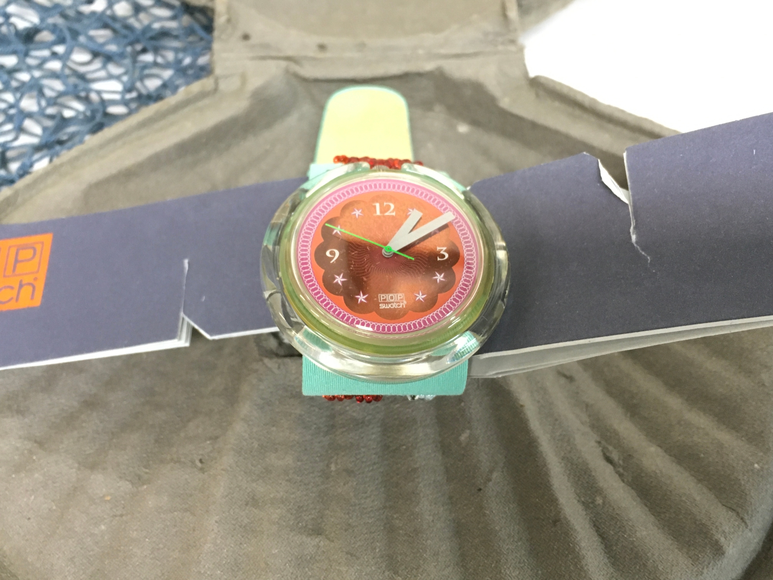 1993 Swatch Pop "Soupe de Poisson" (PWZ106) watch, featuring a pink and orange dial and a clear case. packaged in a specialised grey shell-shaped boxaccompanied by blue fishing netting.