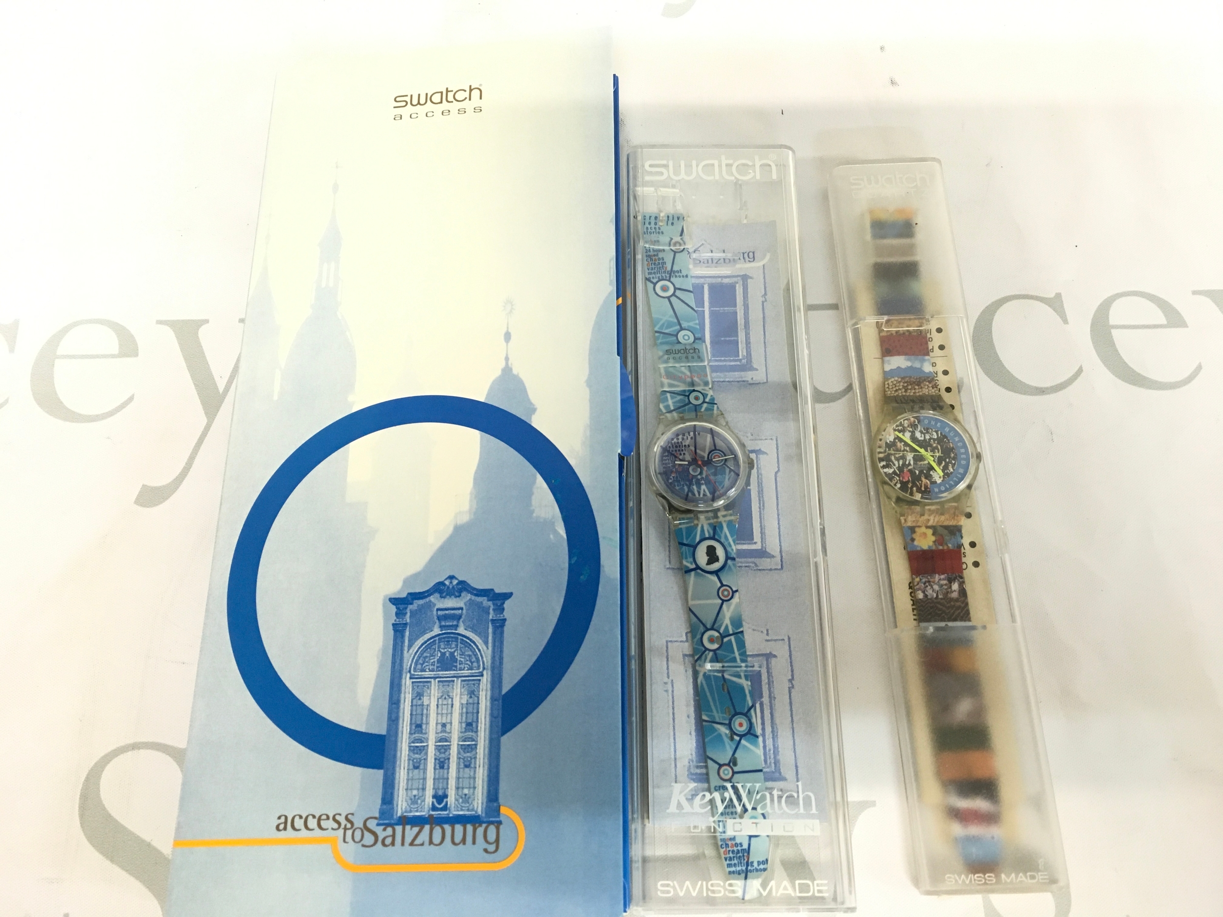 1996 Swatch Access to Salzburg (SKK104) watchfeaturing a blue and white patterned strap. It includes the original "KeyWatch" branded packaging with graphics of the Salzburg cathedral. Also 1992 Swatch "The People" (GZ126) watch, featuring a distinctive crowd photo dial and bright yellow hands.