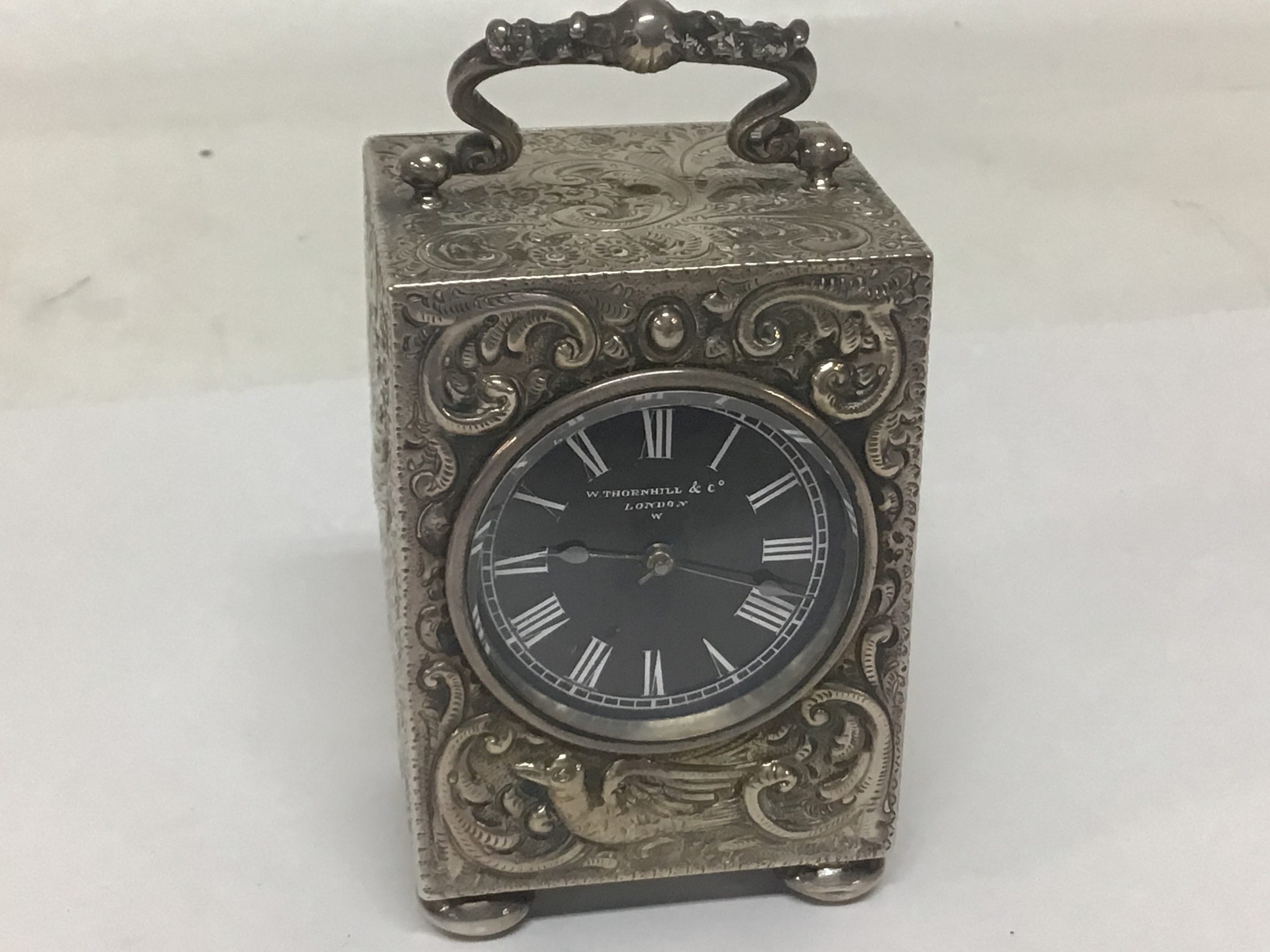  A quality Victorian silver cased travelling clock the case with a perfusion of scrolls and birds  the case with a top handle. The black dial with the inscription W Thornhill & Co London. seen working and with a key Hallmarks for London possibly 1864. Height 8cm 
 