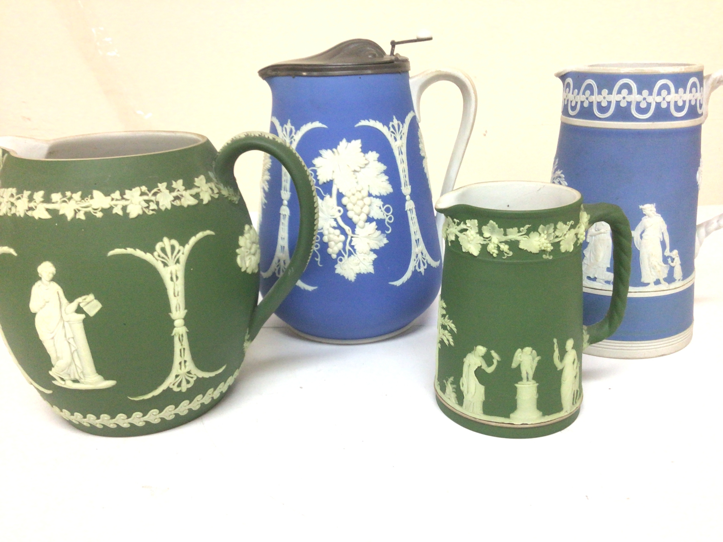  Four late  Victorian Edwardian Wedgwood jugs decorated with raised sprig decoration of classical inspiration Two jugs with Wedgwood stamp one with a pewter lid no obvious damage maximum Hight 22cm (4) 