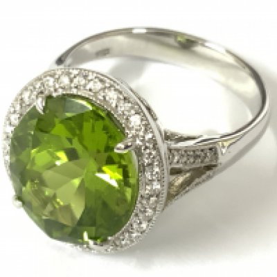 18ct white gold large oval peridot and RBC diamond cluster ring with diamonds to the set split shoulders. Peridot 7.02ct. Diamonds 0.28ct. Approx ring size N/O. Postage category A