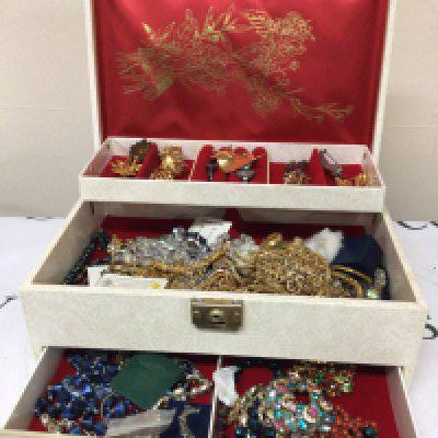 A box containing a collection of costume jewellery including brooches necklace and other oddments.