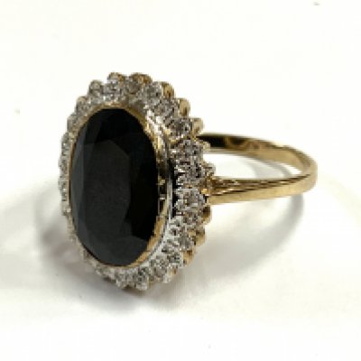 A 9ct gold ring set with a large blue central sapphire and surrounded by small cut diamonds. (A)