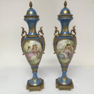 A pair of Sevres style porcelain urn vases with applied gilt metal mounts decorated with rococo influence panels of reclining figures. Height 40cm no obvious damage.