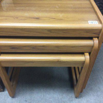 A nest of three modern design teak tables with glass tops .