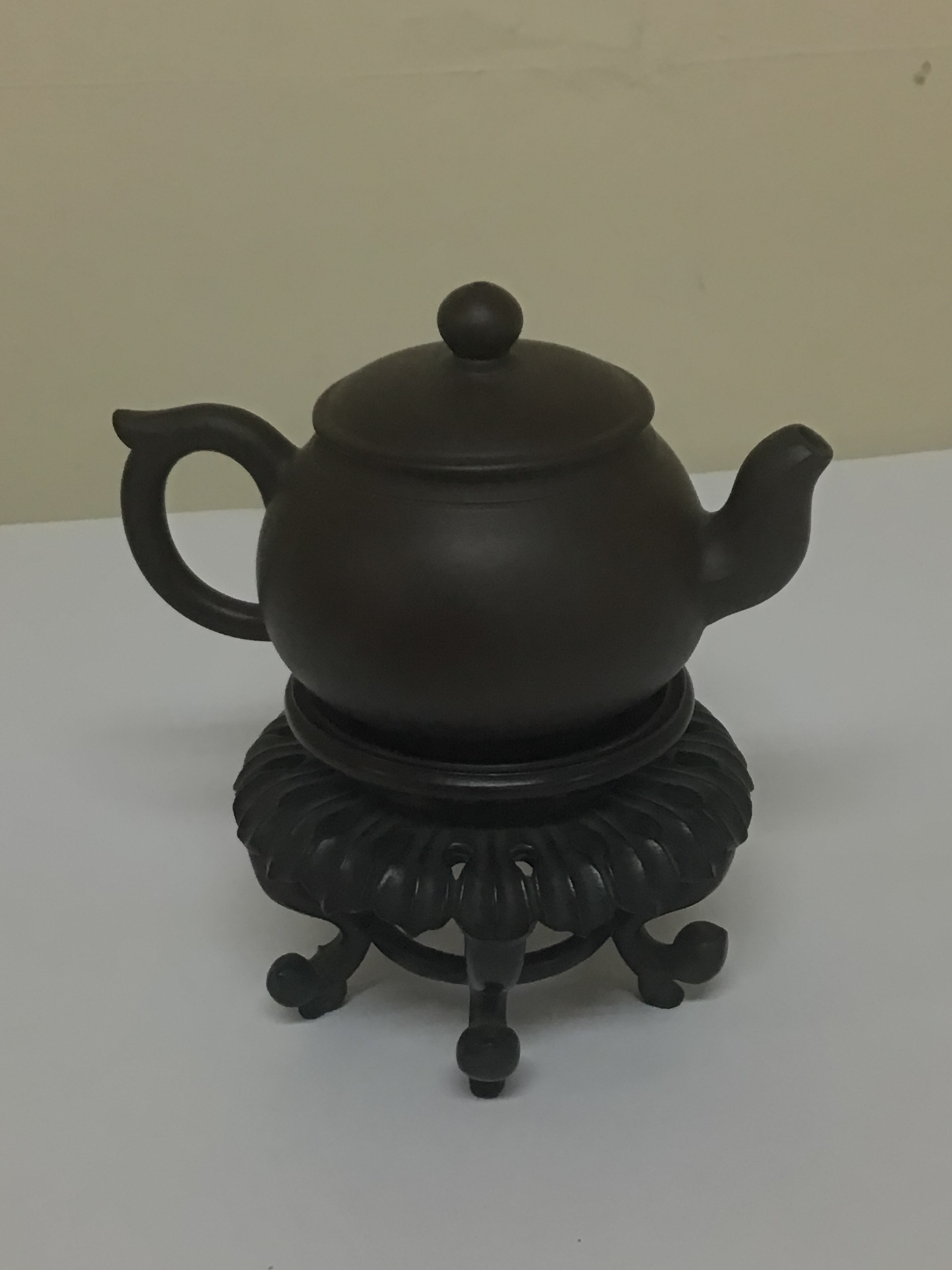 A minute Chinese earthenware tea pot on a hardwood stand the dark brown tea pot with caricature marks to the base no obvious damage. NO RESERVE