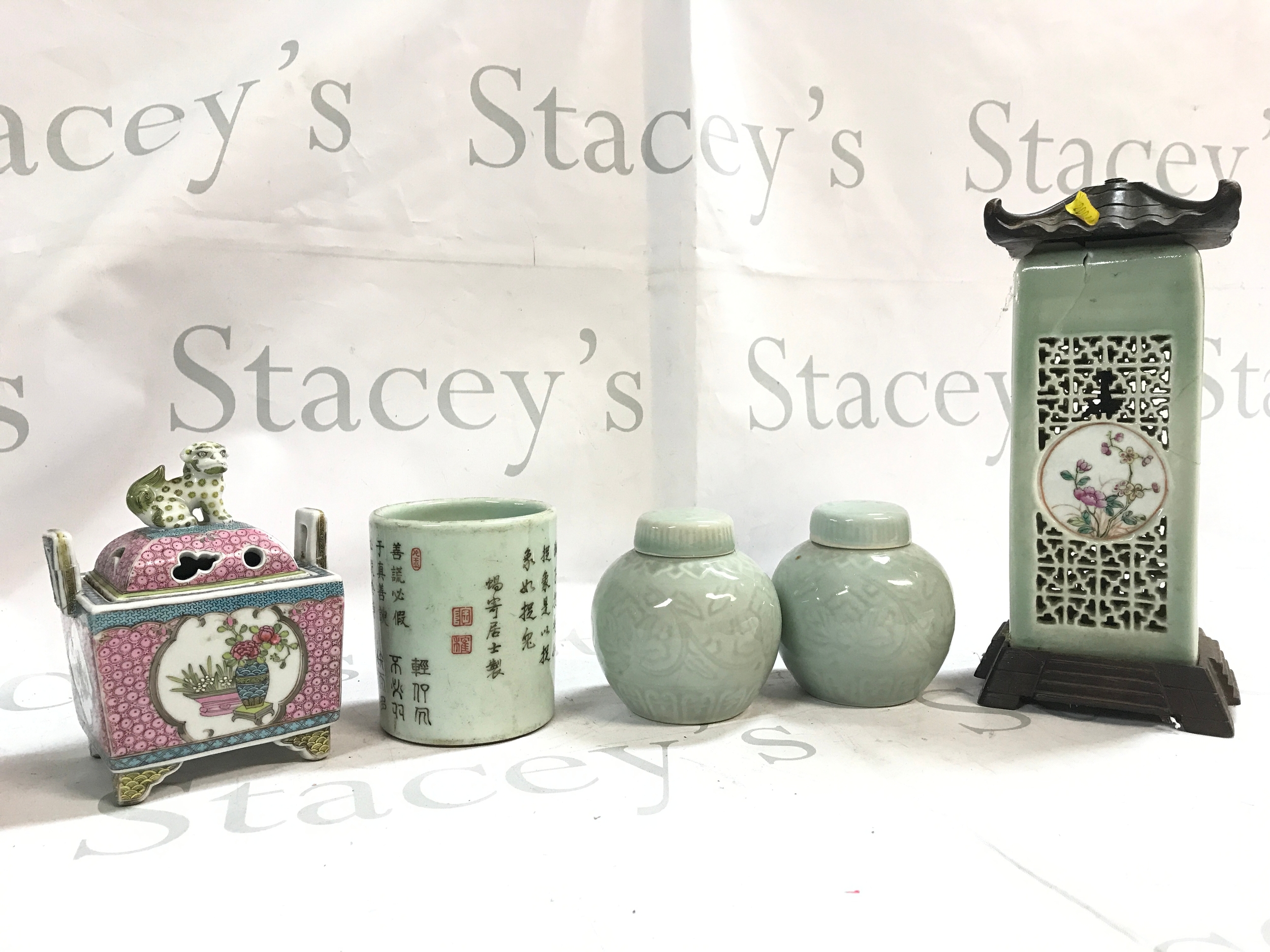 Chinese porcelain items pink famille rose covered censer (15cm tall) with a foo lion finial, a cylindrical brush pot with black Chinese calligraphy, two light green celadon glazed lidded jars, and a tall rectangular celadon openwork lantern-style vase with a dark wooden base and top (26cm tall)