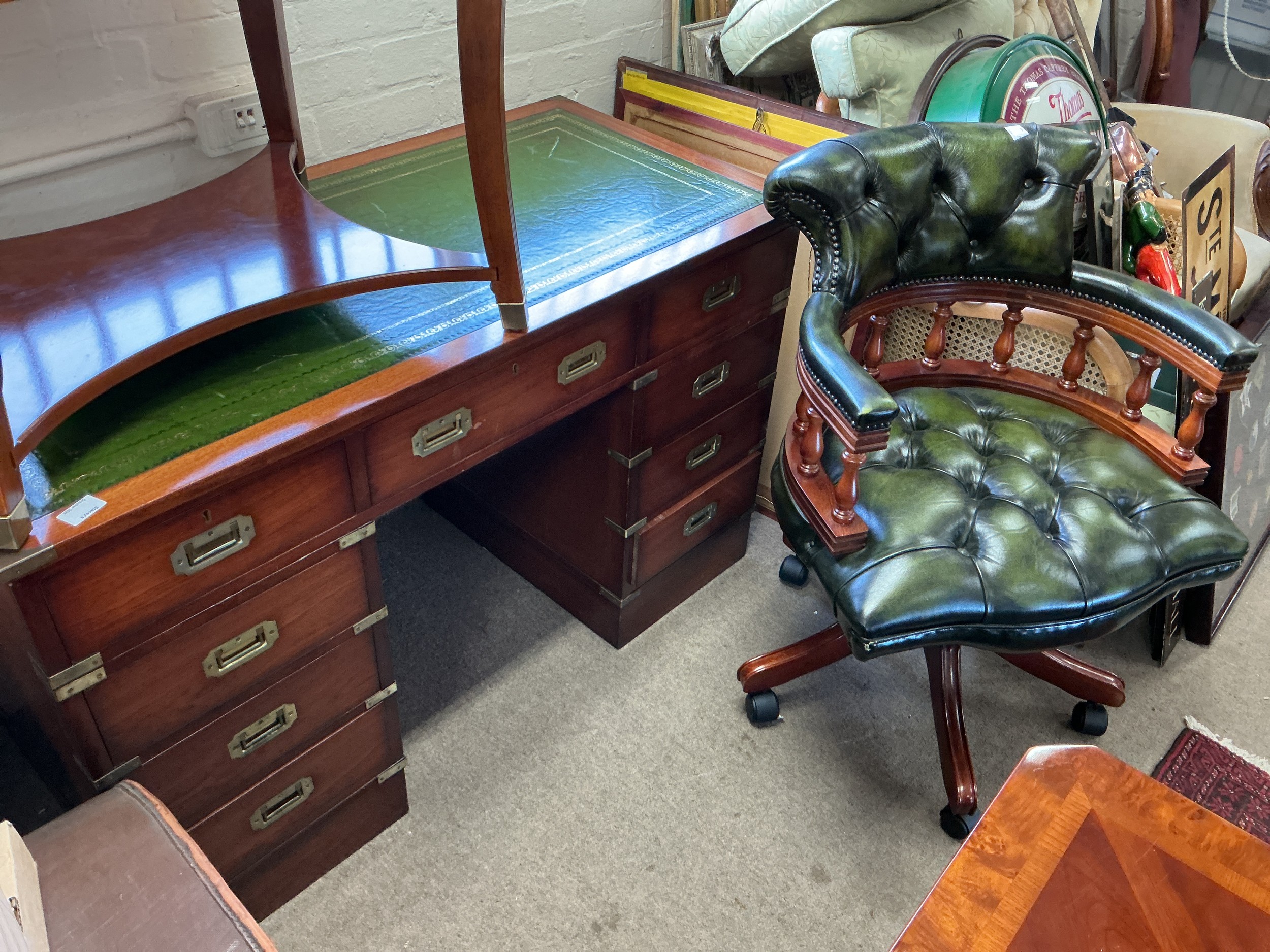A pedestal desk fitted with flush mounted brass handles and a green button back captain's chair.