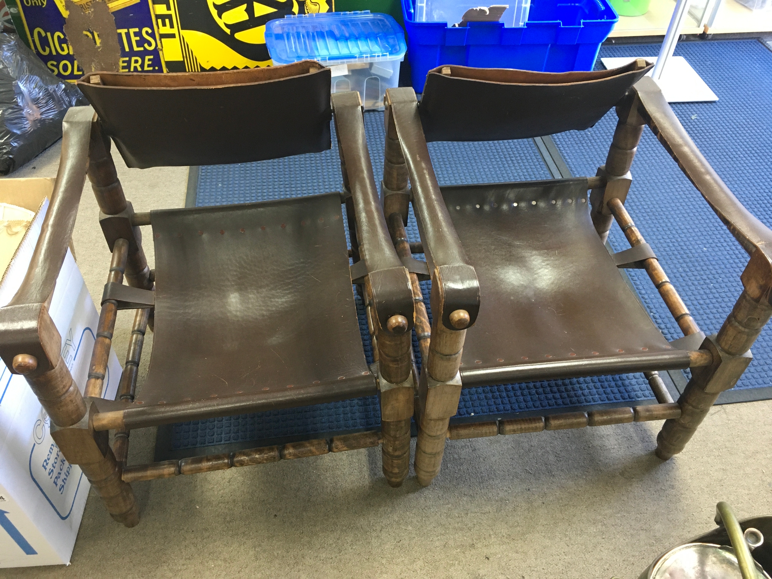 mid century safari style armchairs with carved wooden frames and dark brown sling leather seats and backs