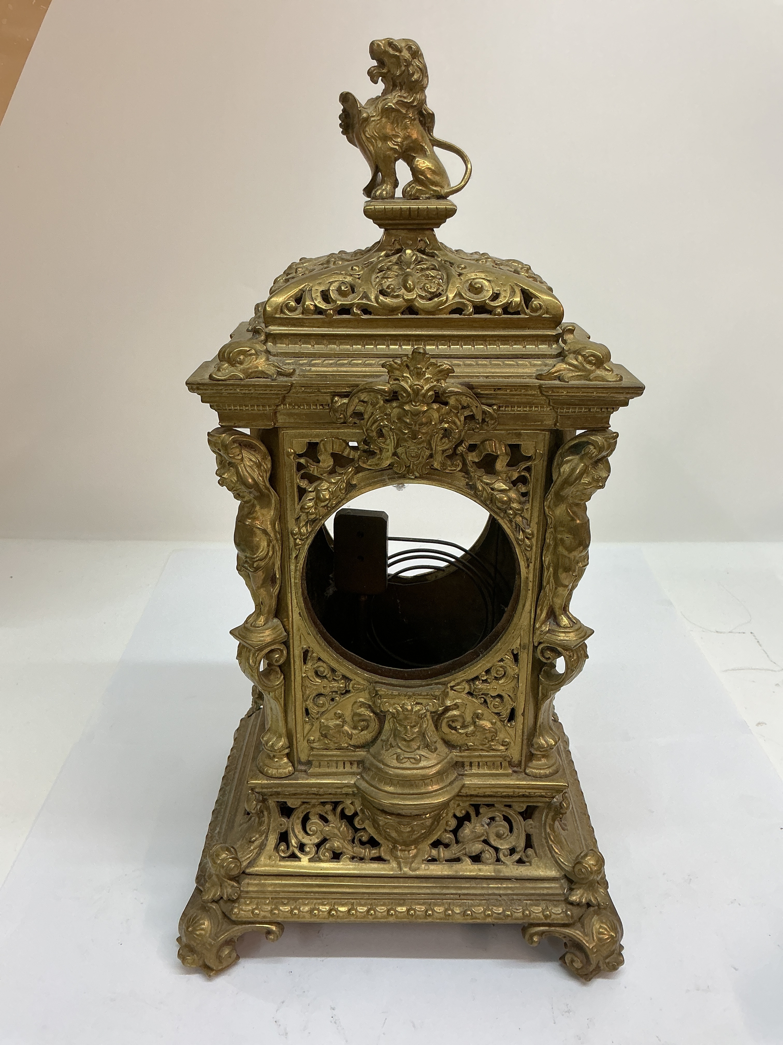 A brass mantle clock case, profusely decorated with scrollwork and figural pillars, surmounted with lion. Approx: W20 x H38 cm