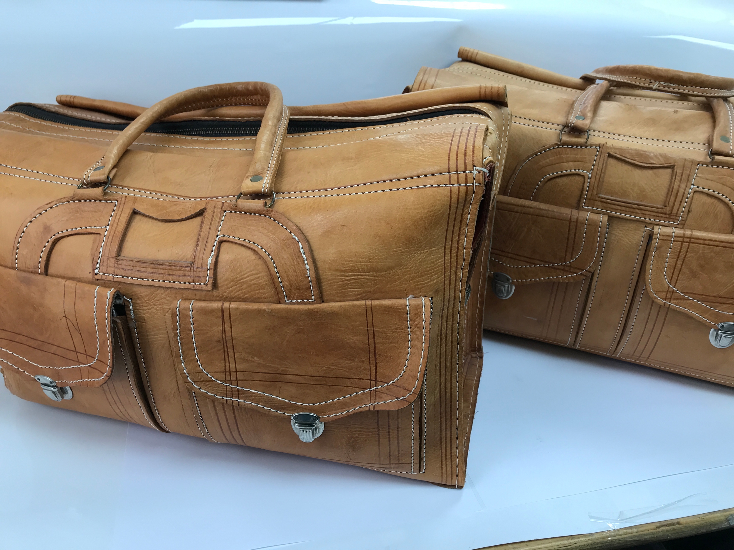 tan leather travel holdall vintage style weekender bag featuring dual front pockets with metal push-lock closures and distinct white accent stitching. 48cm long 32cm tall 23cm wide.