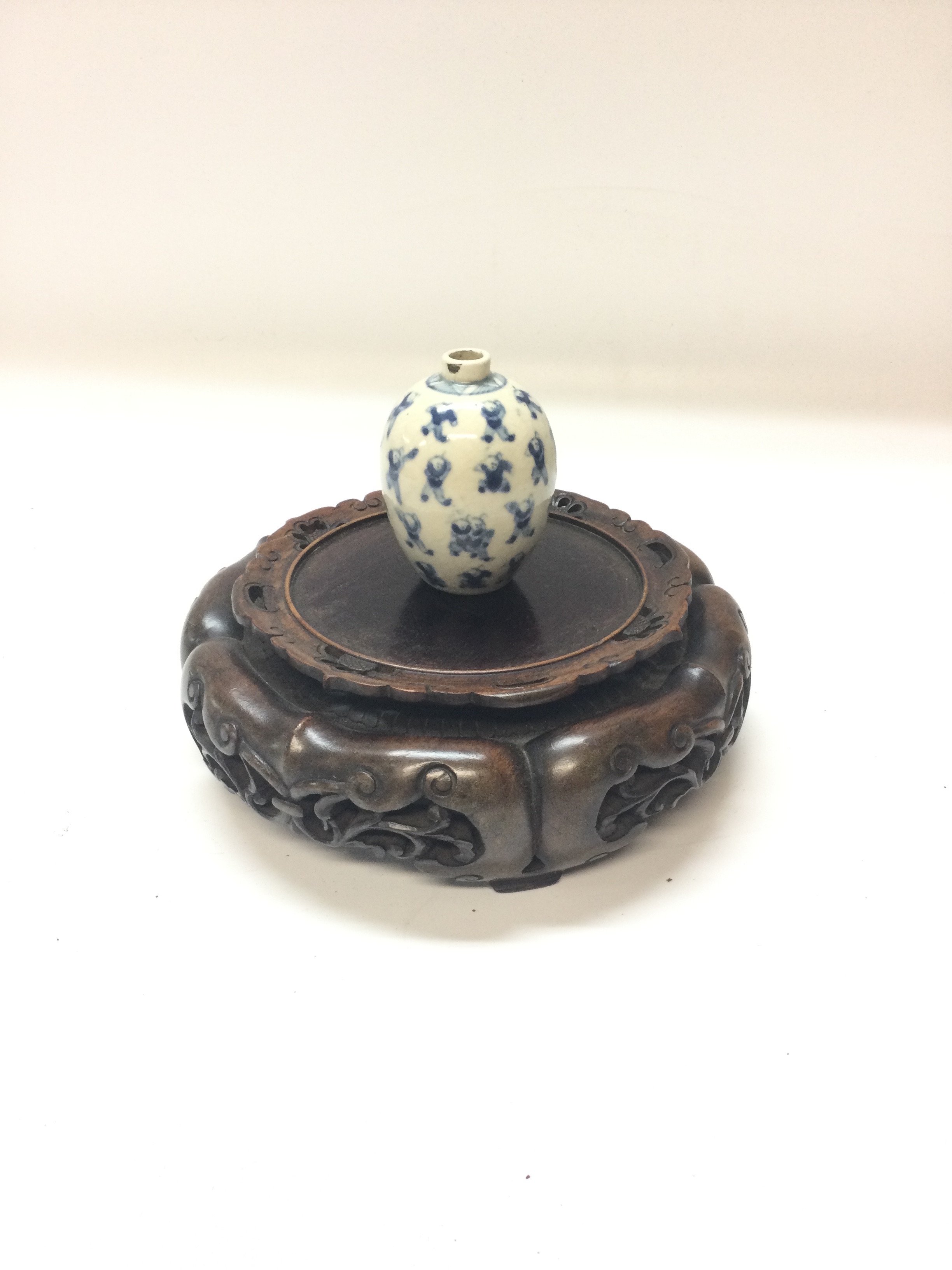 A small Chinese blue and white porcelain vase (8cm) with blue and white figure decoration with a Chinese wooden circular vase base (19cm)
