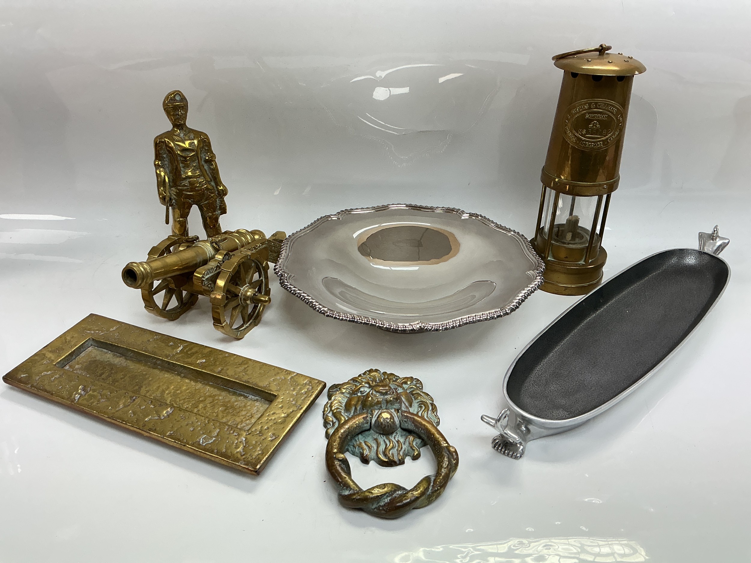 A collection of metalware comprising a Carrol Boyes dish, a brass Thomas & Williams miner's lamp, lion's mask door knocker and other items.