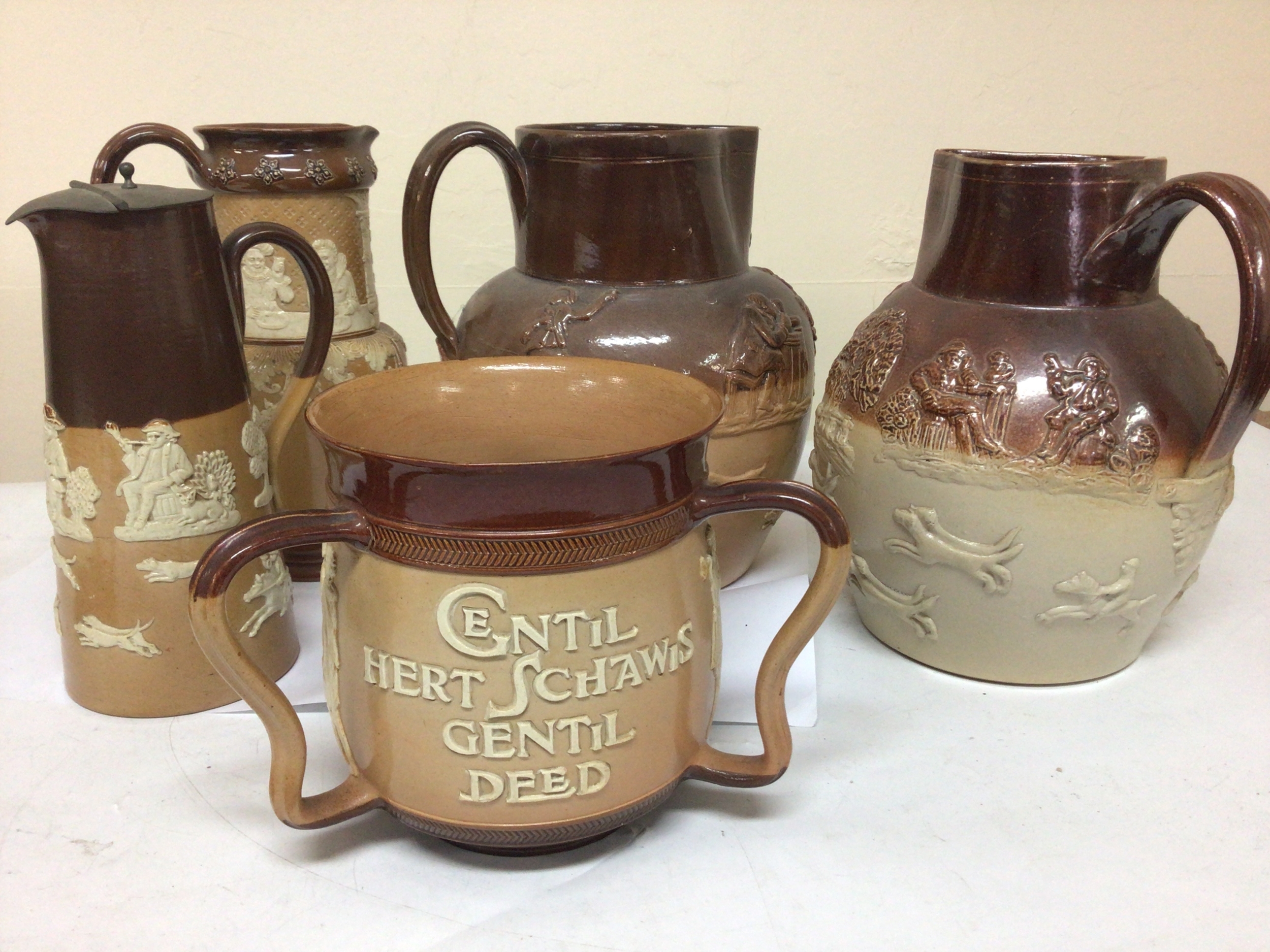 A Lambeth Doulton stoneware loving cup with the Nobel inscription'A Gentle Heart shows a Gentle deed" slight chip to the rim and other Lambeth and Royal Doulton stoneware jugs (5) NO RESERVE