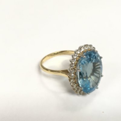 An 18ct white and yellow gold ring set with a large oval faceted blue topaz surrounded by RBC diamonds. Topaz approx 10.00ct, diamonds approx 0.80ct. Approx 8g and approx size N. Shipping category A.