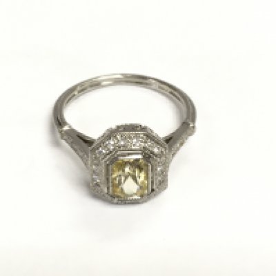 A platinum ring set with a central yellow sapphire surrounded by R/C diamonds with diamond set shoulders and filigree detailing. Yellow sapphire approx 1.24ct and diamonds approx 0.20ct. Approx 3.3g and approx size M. Shipping category A.