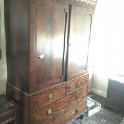 A late George III mahogany linen press with a cornice above cupboard door enclosing sliding shelves above two short and two long drawers on turned legs Height 215cm