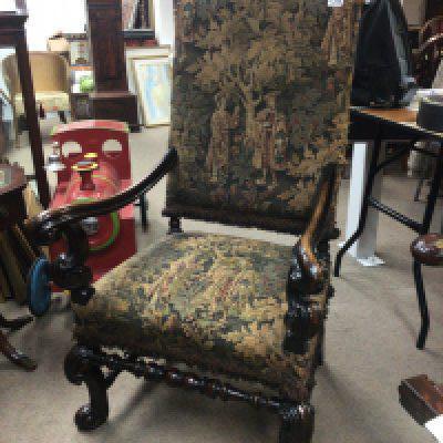 A Charles II style chair with a carved top rail above pictorial tapestry upholstery with scroll arms and legs. good condition.