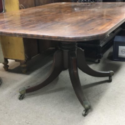 WITHDRAWN- A George III mahogany tip action dining table with a cross-banded edge on splayed inlaid legs terminating in brass cap and caster 148cmx100cm