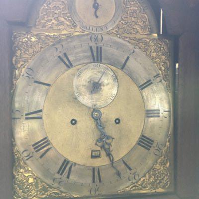 A oak carved long case clock the arched brass dial with Roman numerals.