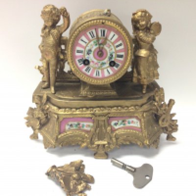 A French gilt mantle clock with children figures and pink floral panel designs. Damaged and in need of restoration. This lot cannot be posted