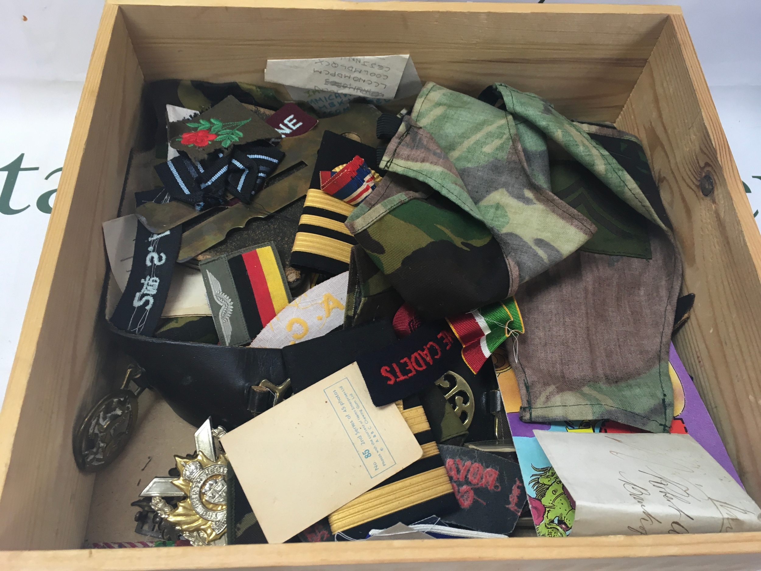 This wooden box contains a mixed assortment of military insignia, textiles, uniform parts, and small ephemera, representing various nations and eras. 