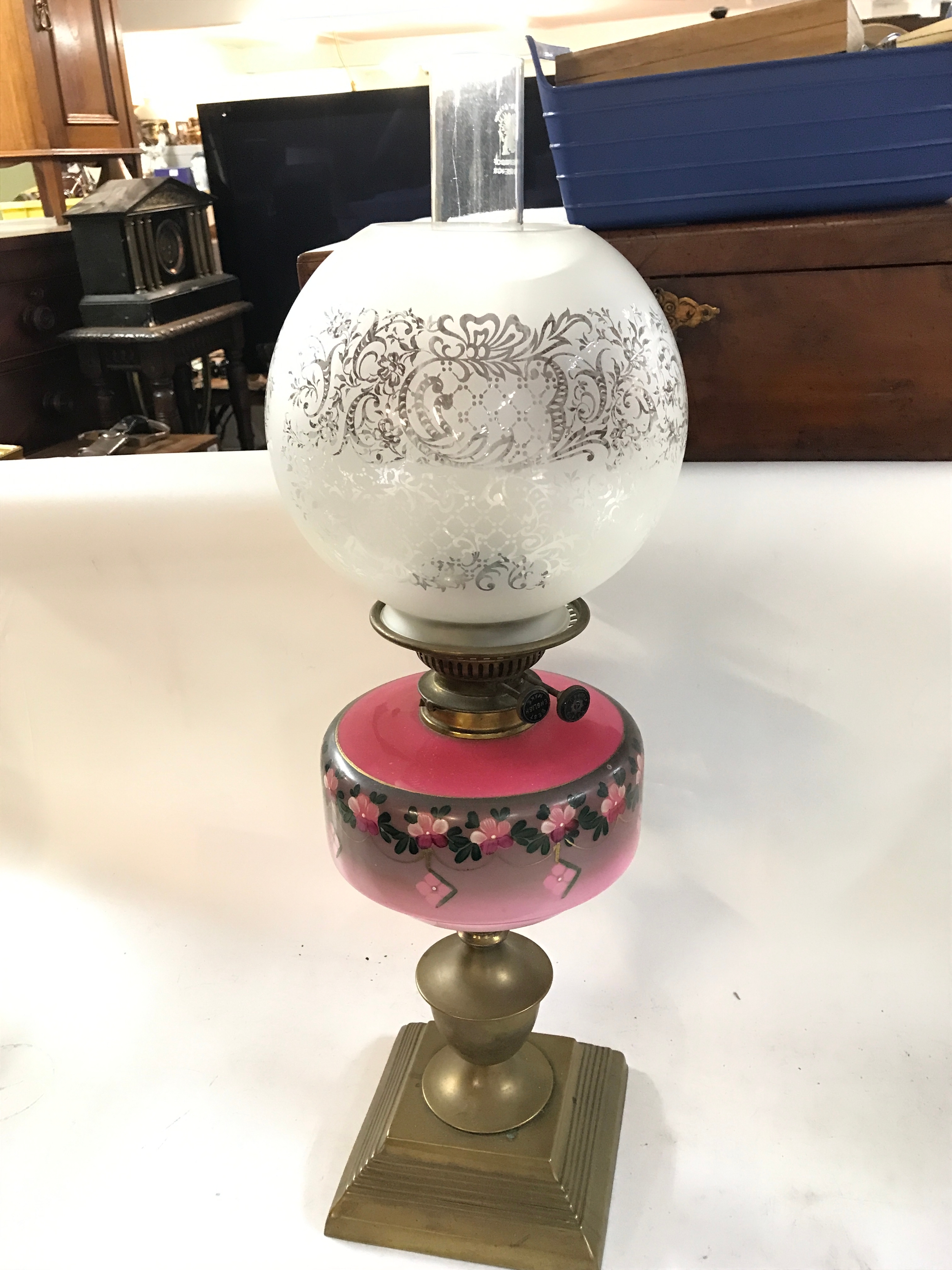 A late 19th-century Victorian oil lamp featuring a brass base, a pink glass font with hand-painted floral decoration, and an acid-etched frosted glass globe shade with a clear glass chimney, 64cm tall 