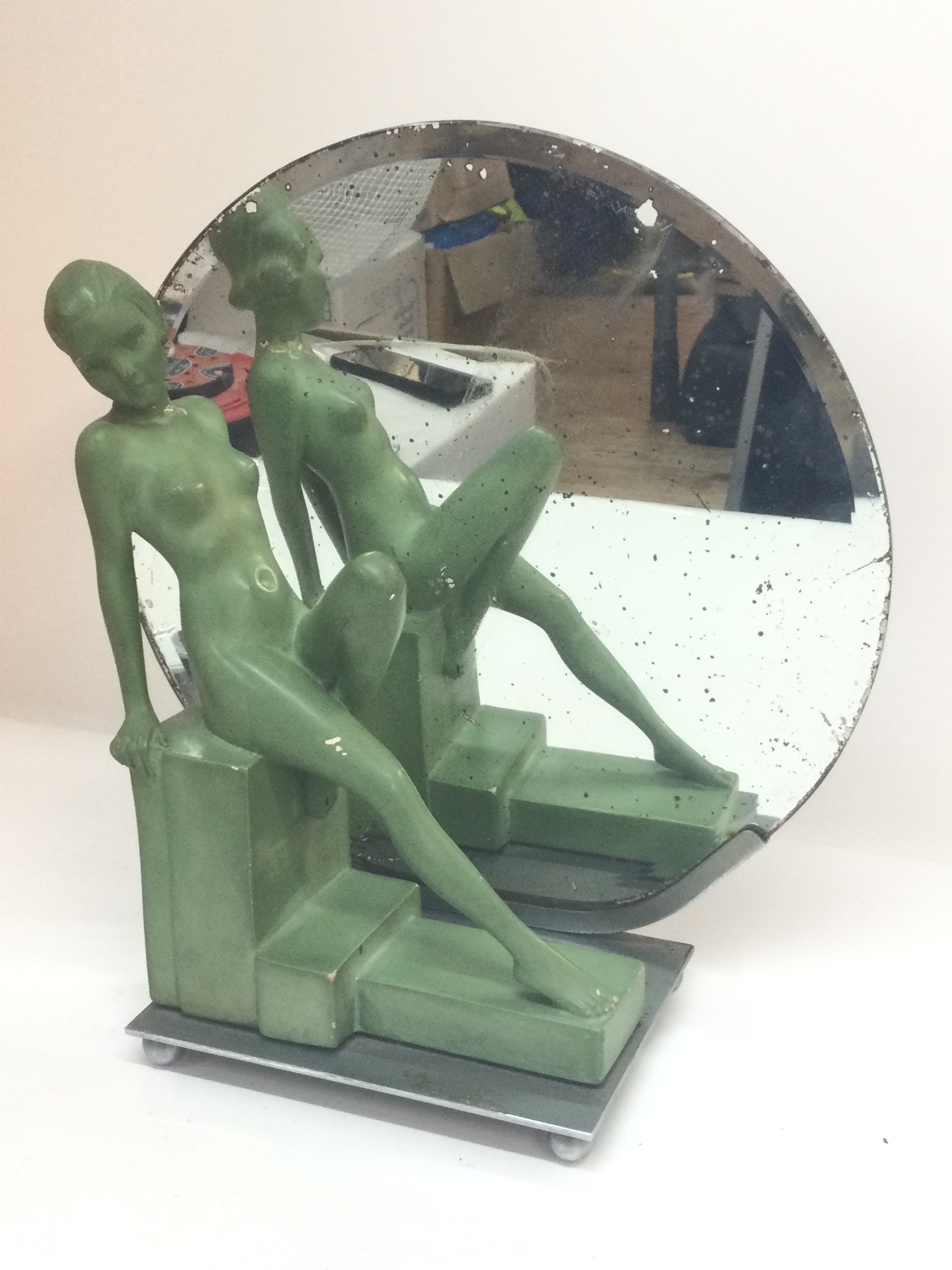 An Art Deco figure, a seated female figure with a green patina finish and a circular mirror, 38cm tall 36cm wide