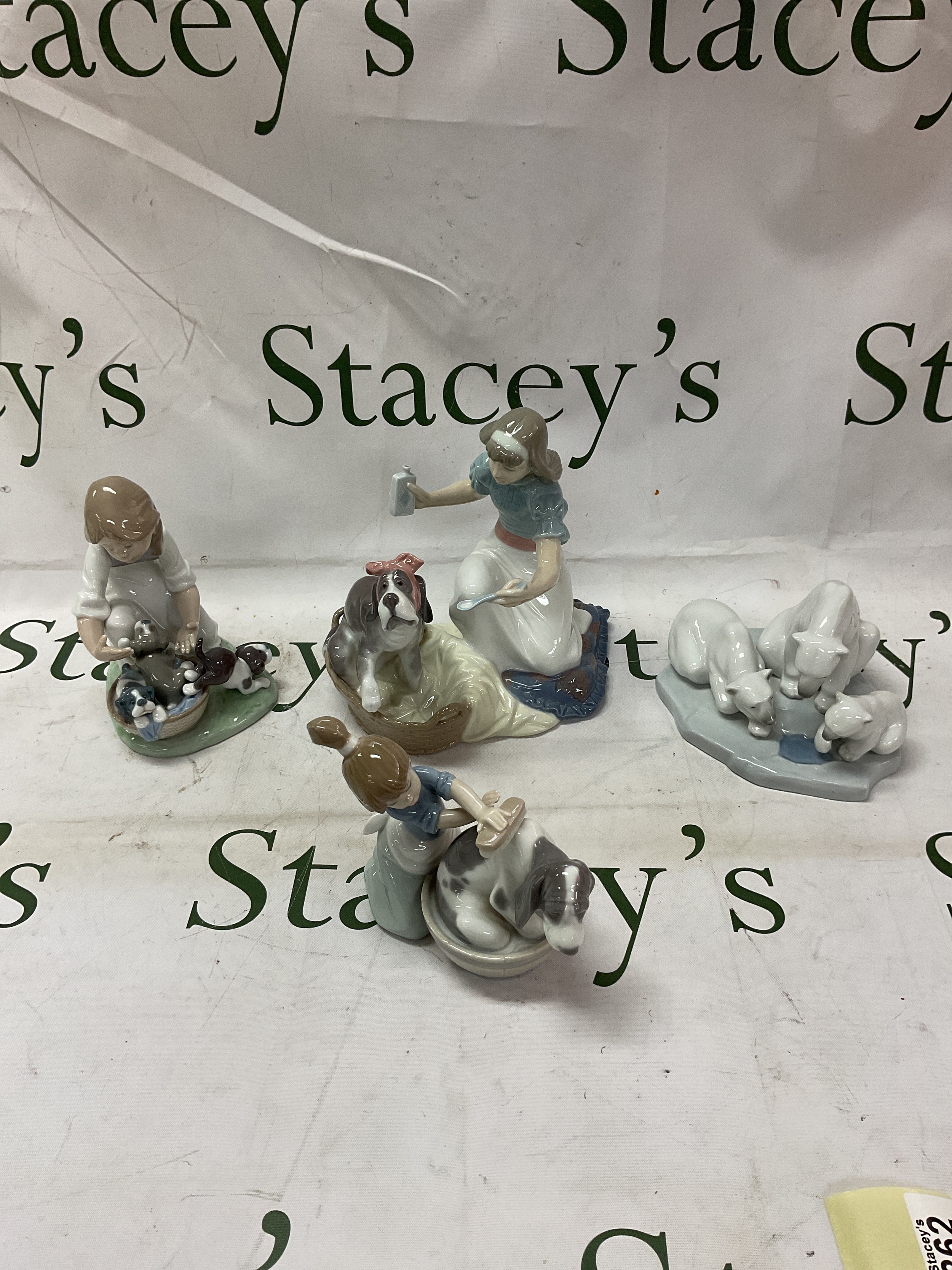 Four Lladro figurines, three bears, dog being bathed, girl with basket of puppies and girl giving medicine to a poor hound.