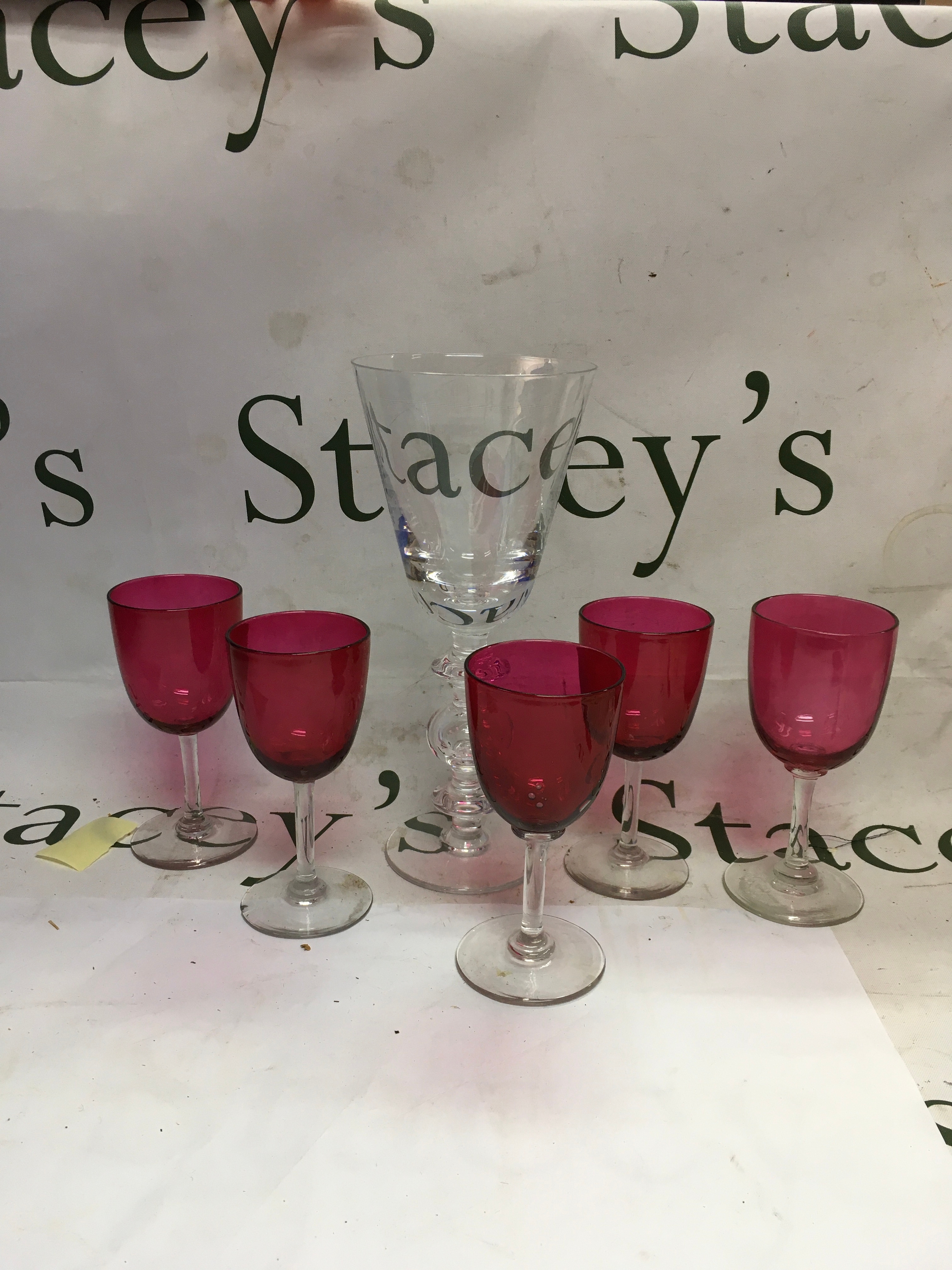 A set of antique Victorian glassware. Featuring a mix of cranberry glass stemmed tableware and a large central clear glass goblet. 