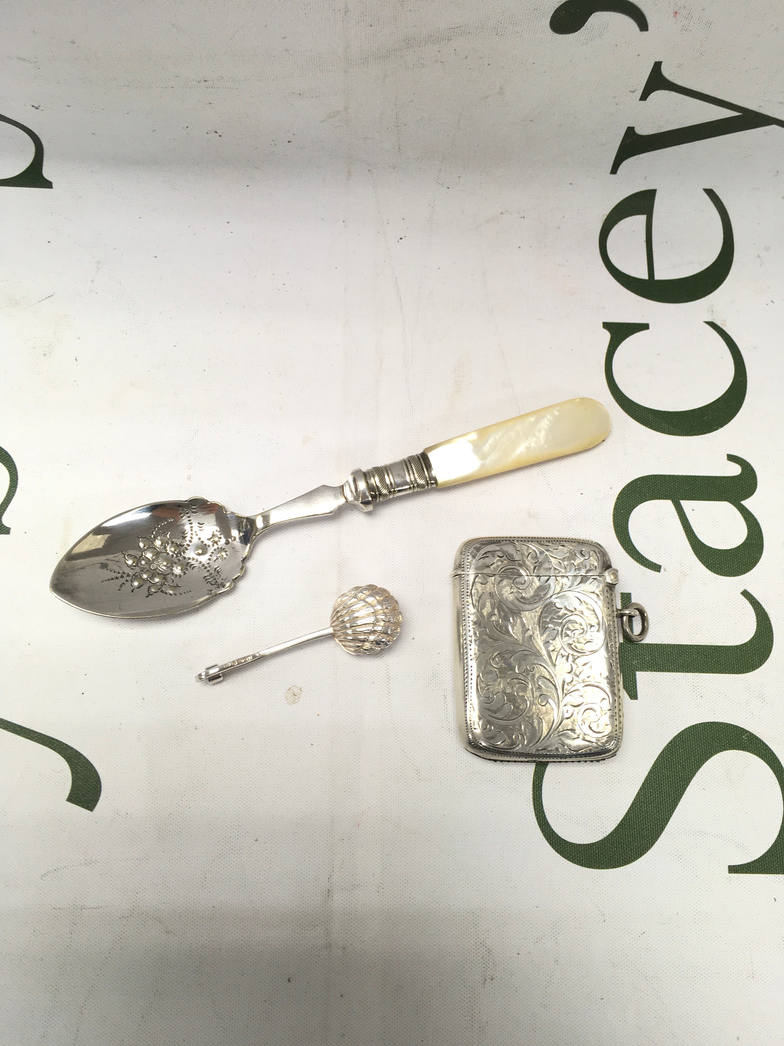 A small collection of silverware including a spoon, napkin holder and a match box.