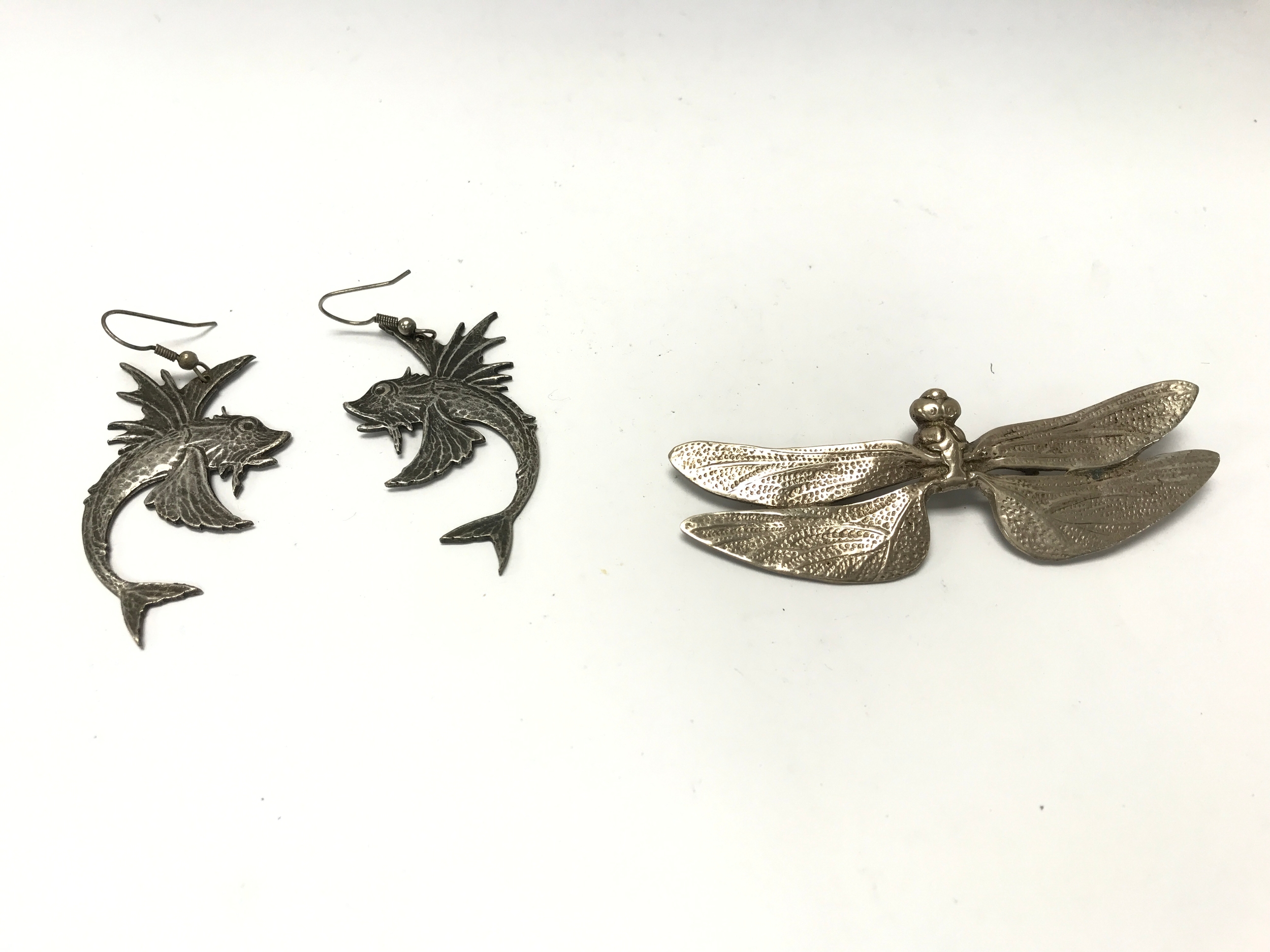 silver dragonfly pin or brooch with intricately textured wings. dangle earrings feature a textured flying fish design with an oxidized silver finish. Neither item is hallmarked. approx 30g