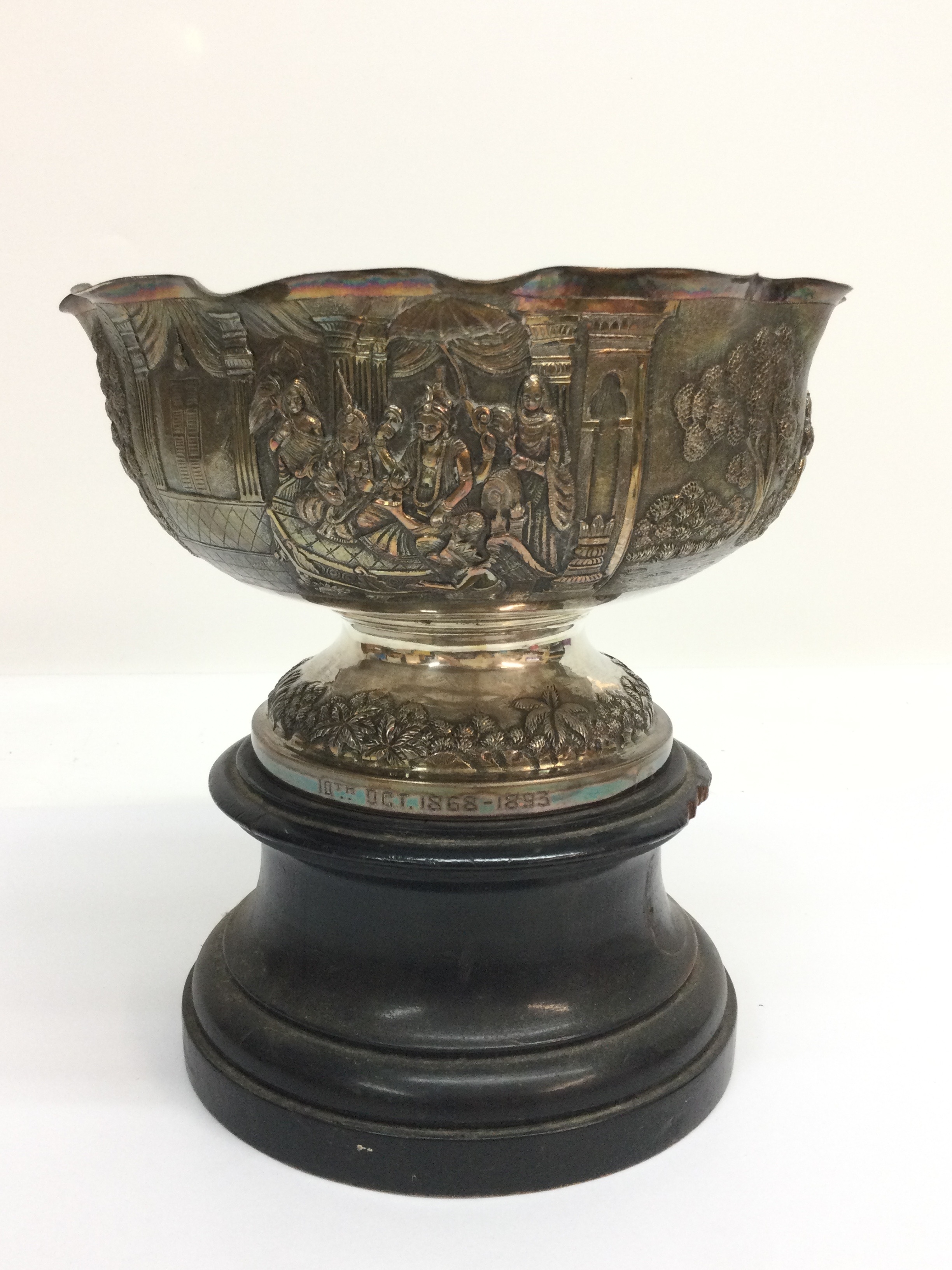 An Indian white metal bowl, repoussee decorated with regal figures and crimped rim.Date engraved to base, on wooden stand. Approx 20 x 13cm
