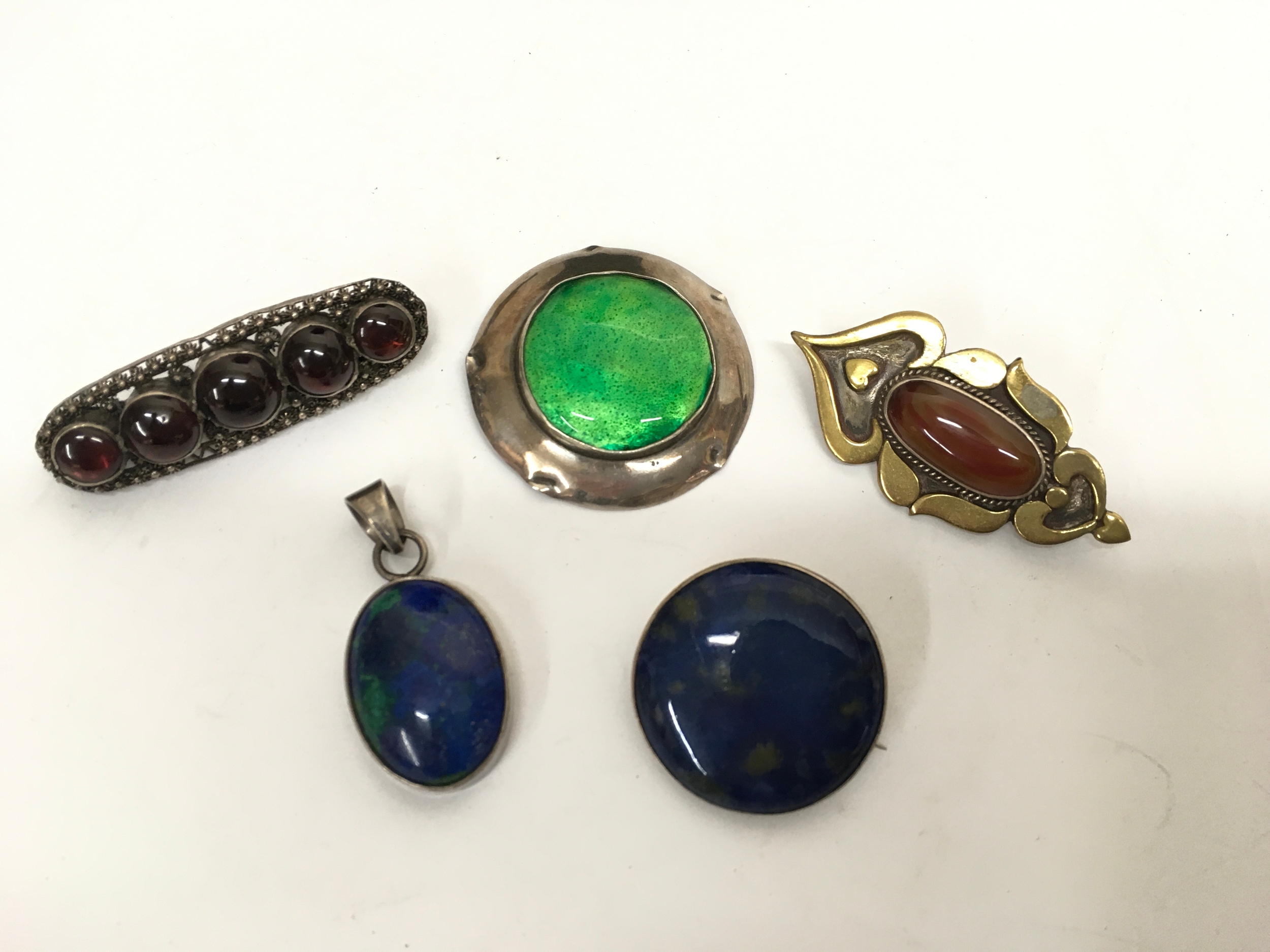 A group of largely silver mounted brooches including a green enamel and stone set examples