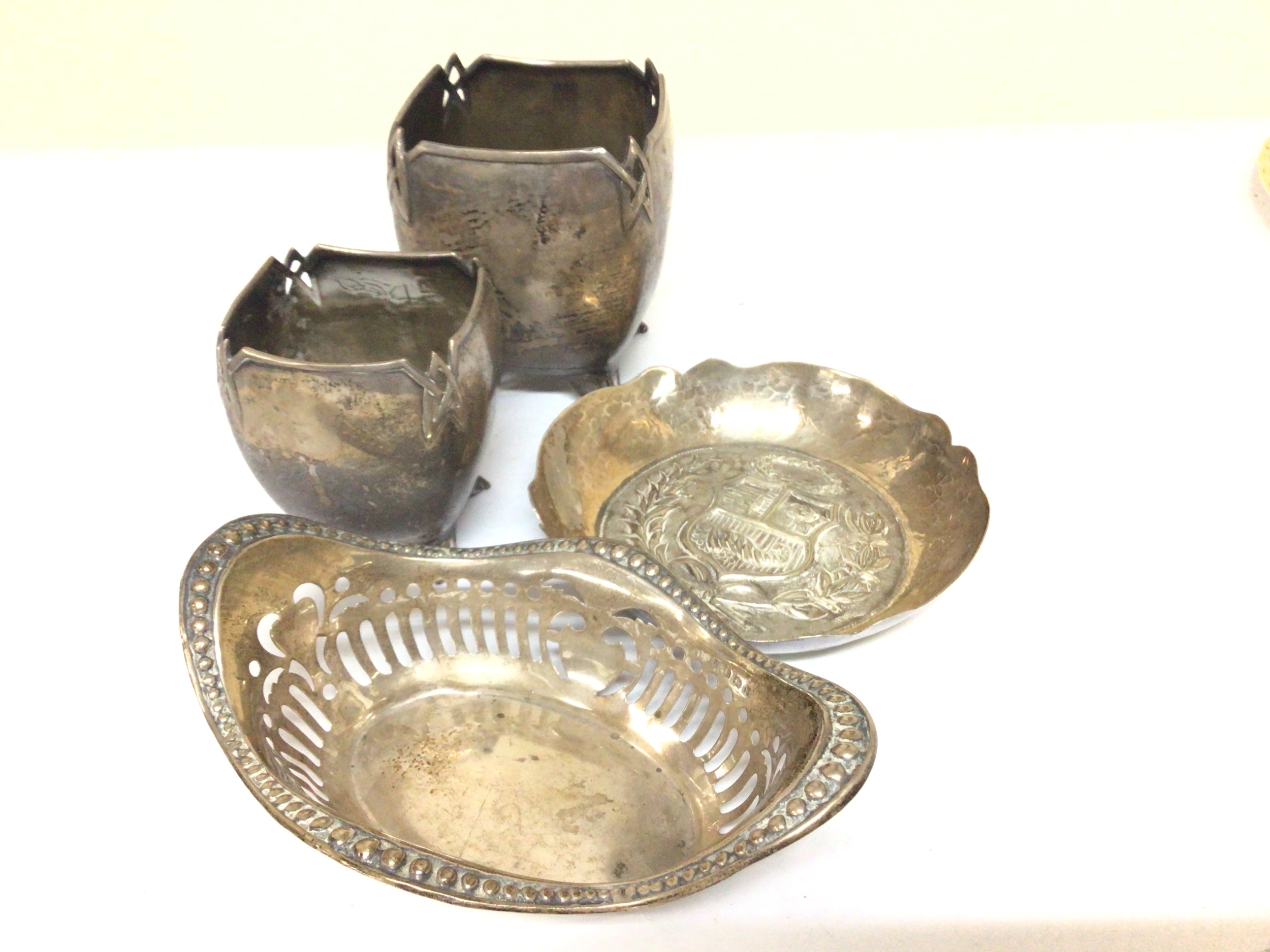 A small silver basket Birmingham hallmarks a Continental white metal dish chased with a coat of Arms and two graduating white metal vessels (4) 