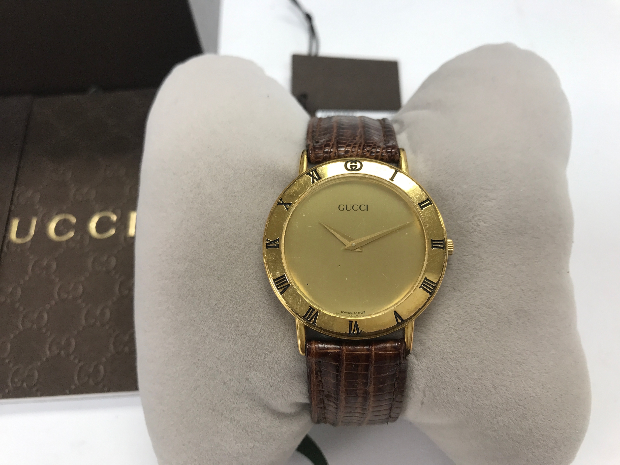 vintage Gucci quartz wristwatch featuring a round gold-tone dial with Roman numerals engraved on the bezel and a brown leather strap. Boxed.
