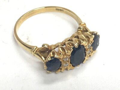 An 18ct stamped gold ring set with three blue sapphires and white stones. Approx weight 5.27 grams, ring size R.