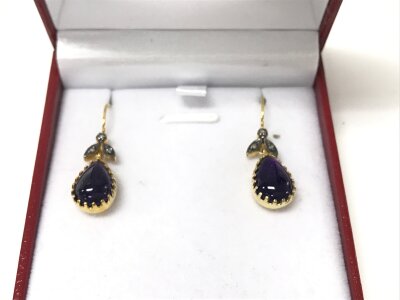 A pair of 9ct yellow gold and silver drop earrings with fish hook backs set with cabochon pear shaped amethyst's and diamond set foliate bales.