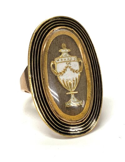 An early Georgian unmarked gold and enamel mourning ring,  hair locket overlaid with a gold and white enamel urn and rock crystal. 6.8g