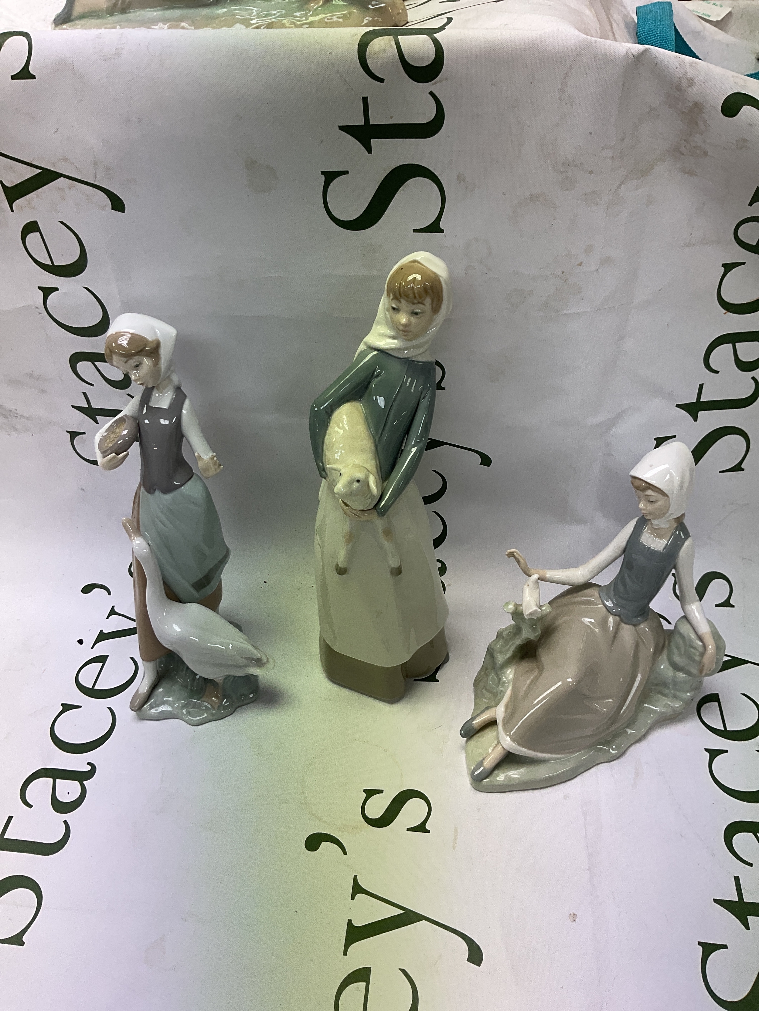 Three Lladro lady figures, one holding a lamb, one with a goose the other seated with a bird.
