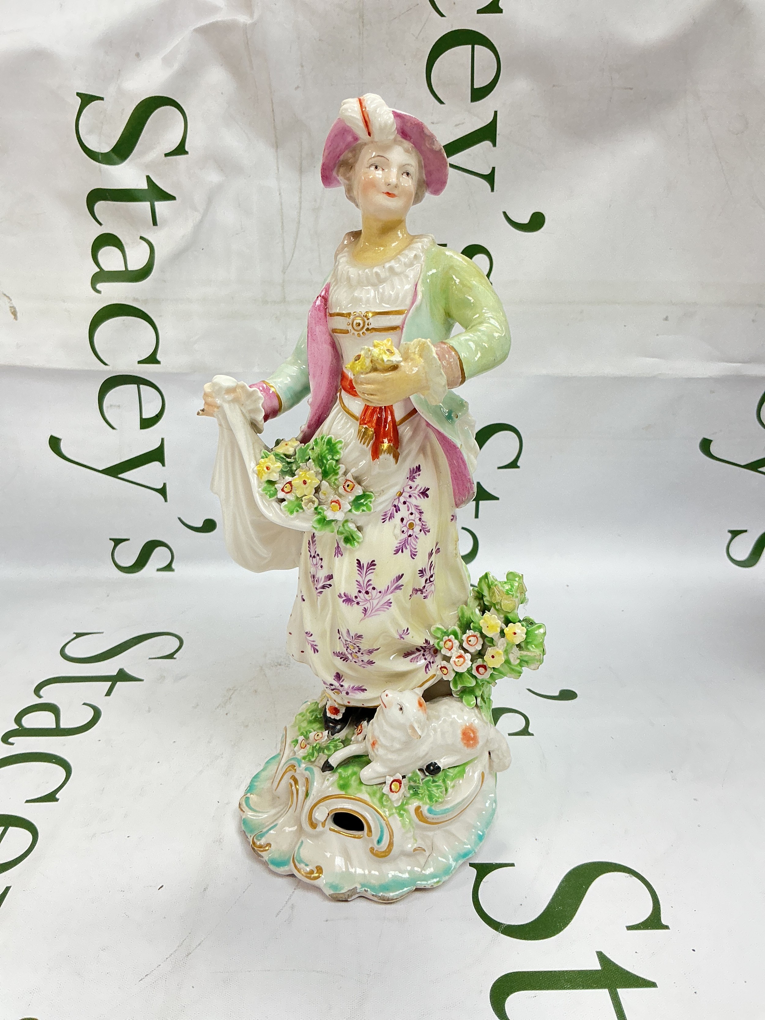 A circa 1760s Derby figure of a " Dresden Shepherdess" with a lamb at her feet and her apron full of flowers and standing on a rococo base. Patch marks Incised G, approx height 26cm. Some restoration and chips.