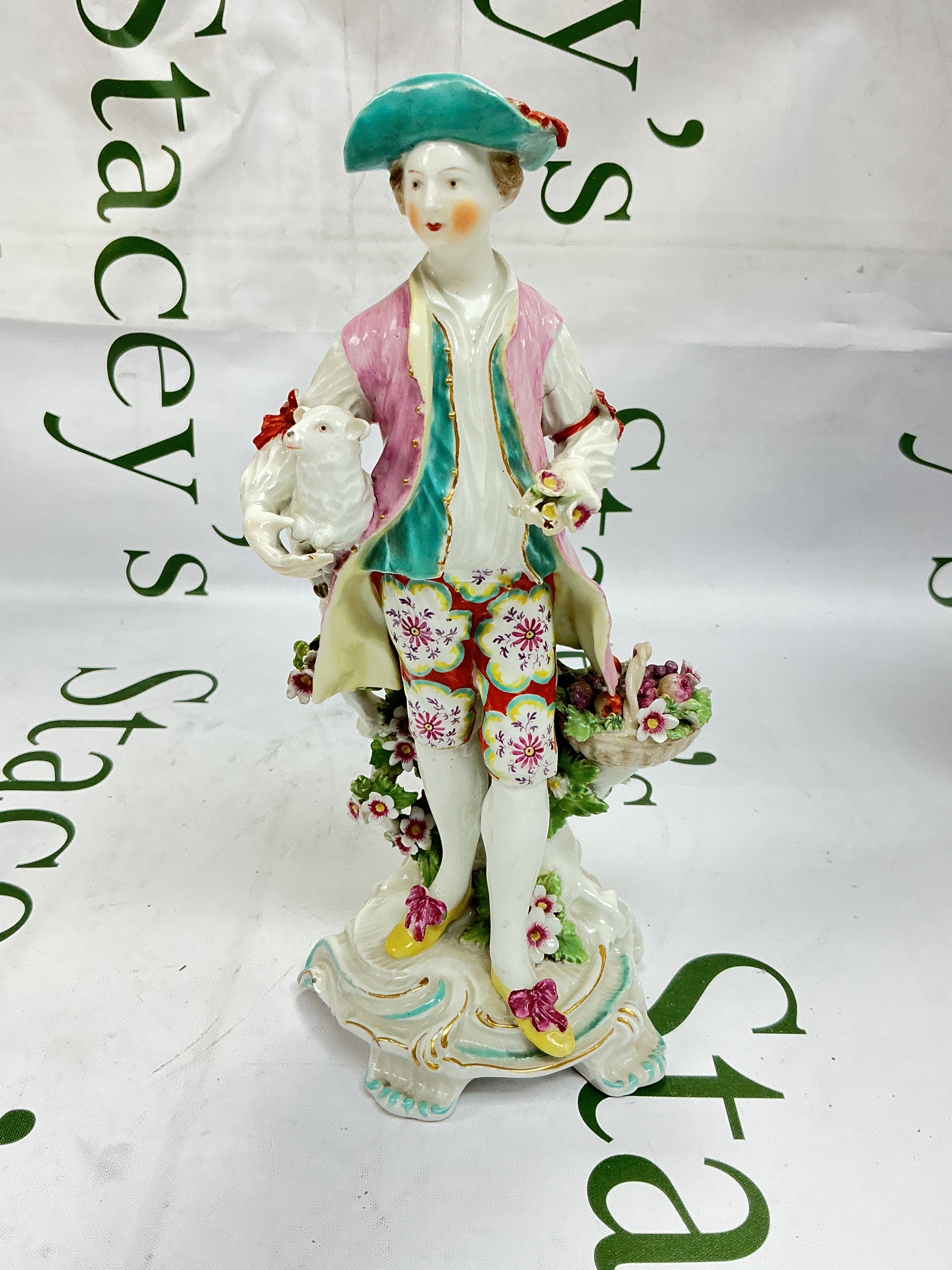 A circa 1760s Derby figure of a shepherd, standing and holding a lamb under one arm and a posy in the other and raised on a turquoise and gilt edged base, approx height 22cm. Some chips and restoration.